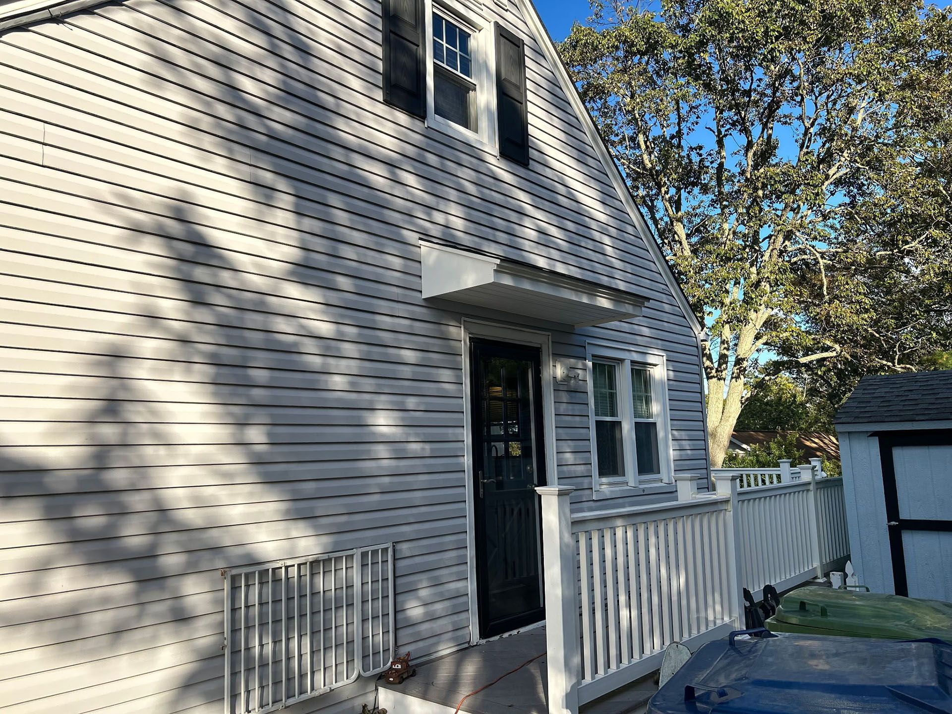 Gray-sided house with a dark door, small porch, and white railing, under a clear blue sky.