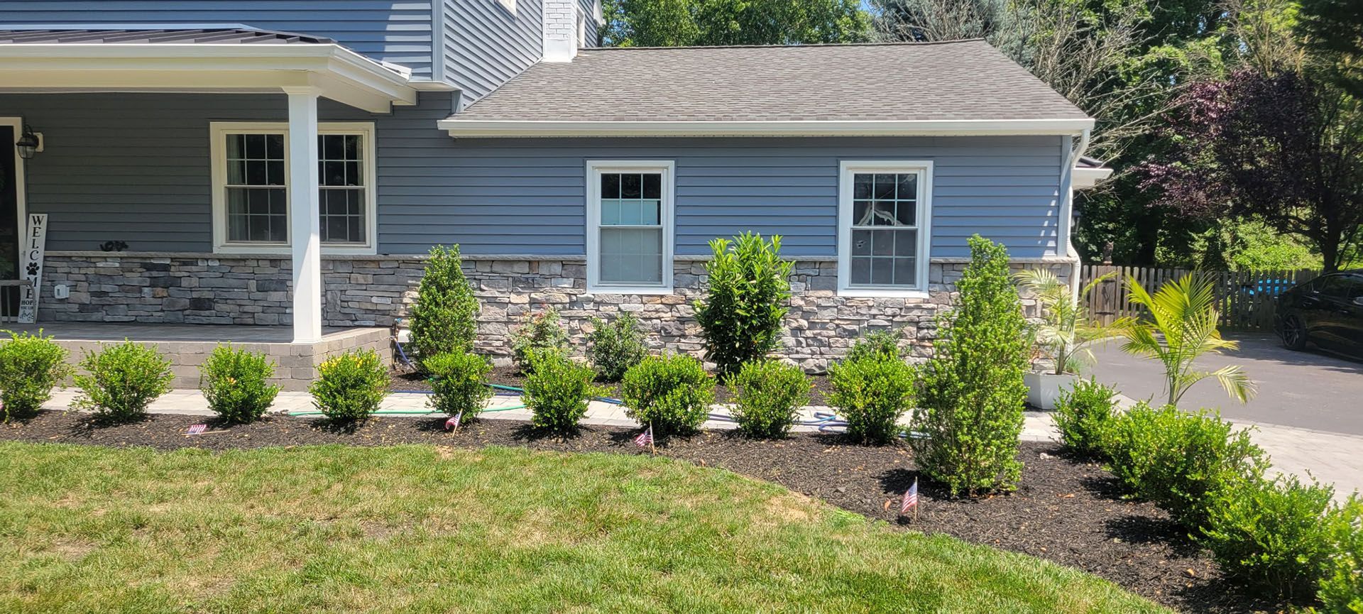 Blue house with gray stone base, trimmed with small green shrubs and grass.