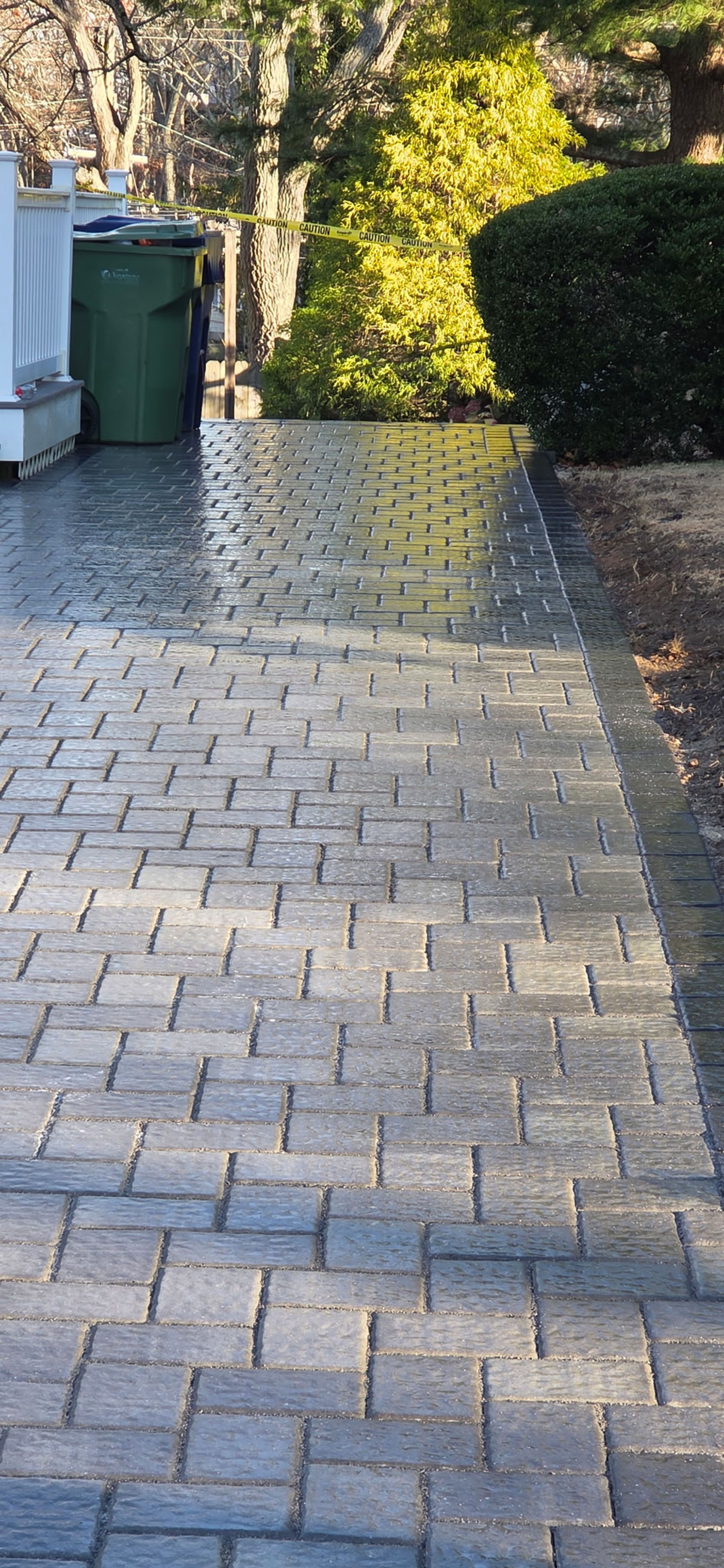 Brick paved pathway leading towards greenery and a trash bin.