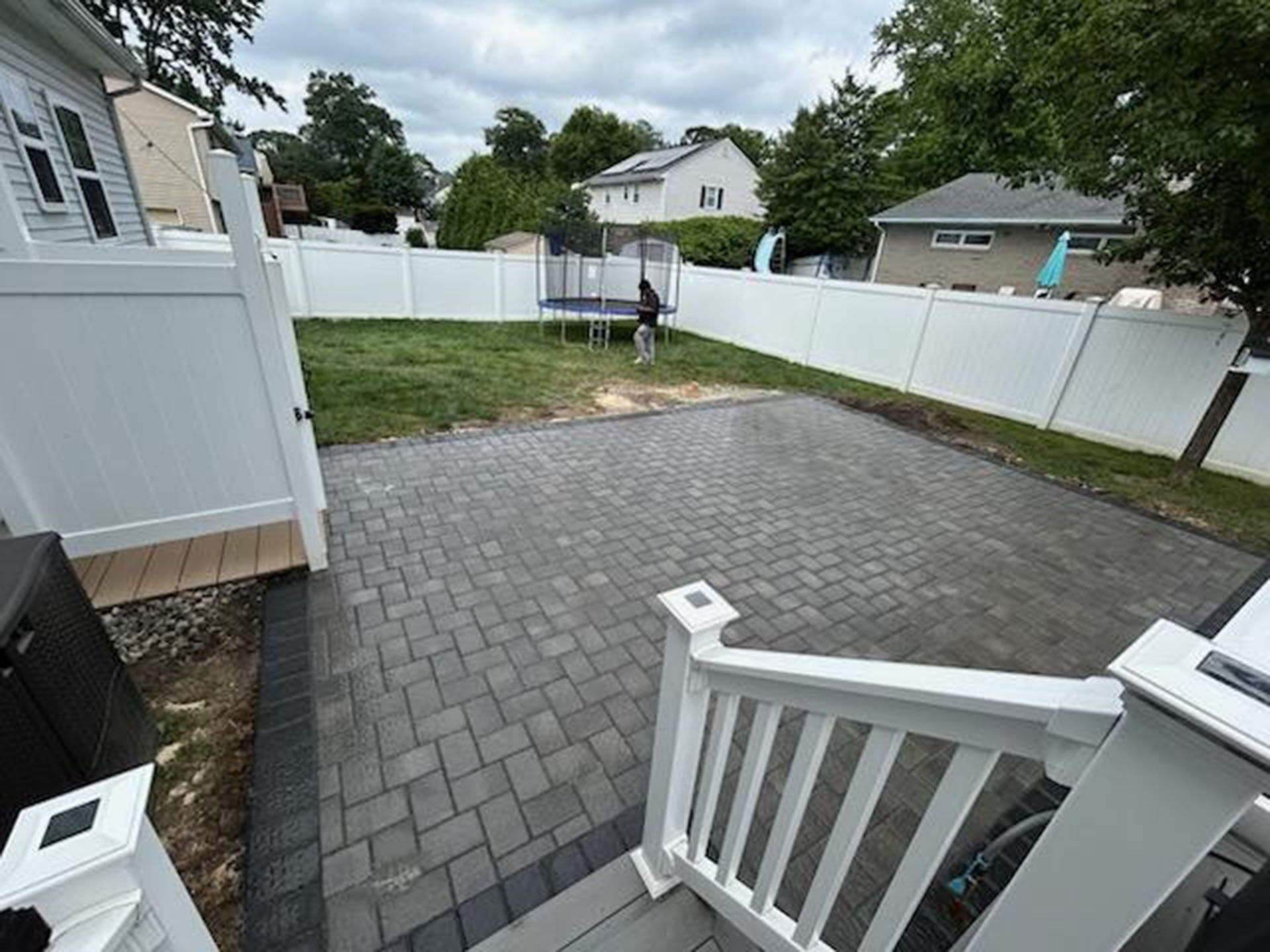 Paver patio and fenced backyard with a trampoline and small dog.