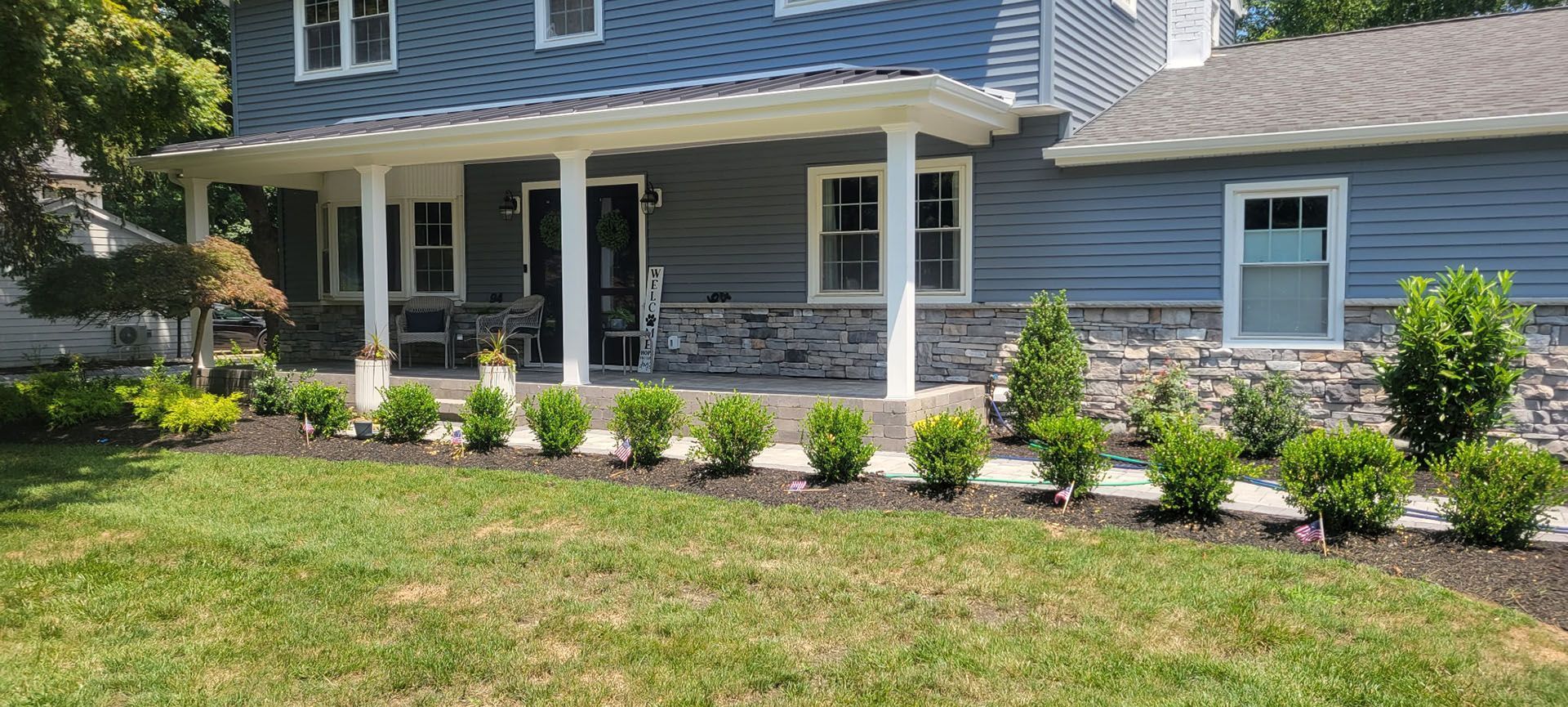 Blue house with white columns and a small garden with green bushes.
