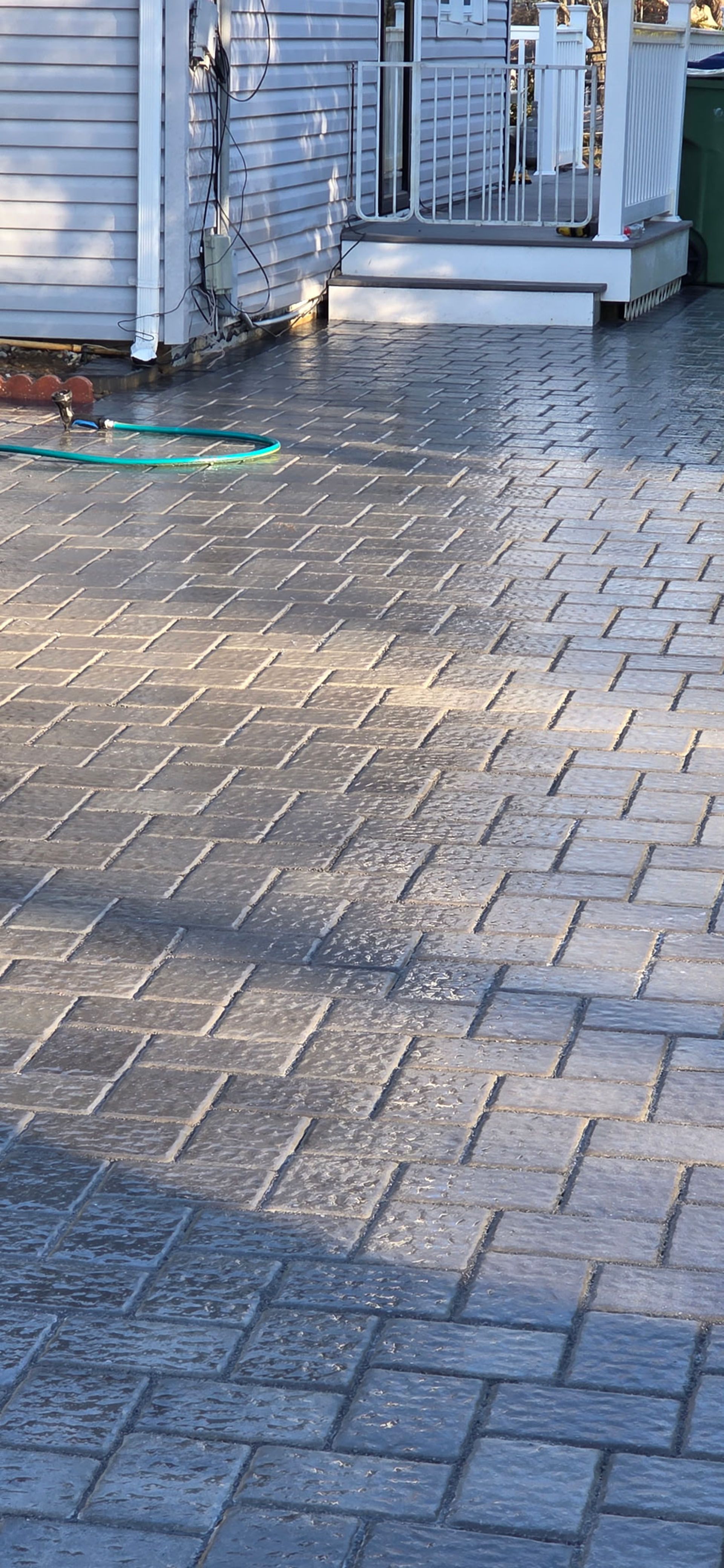 Wet brick driveway leading to a white porch and building.