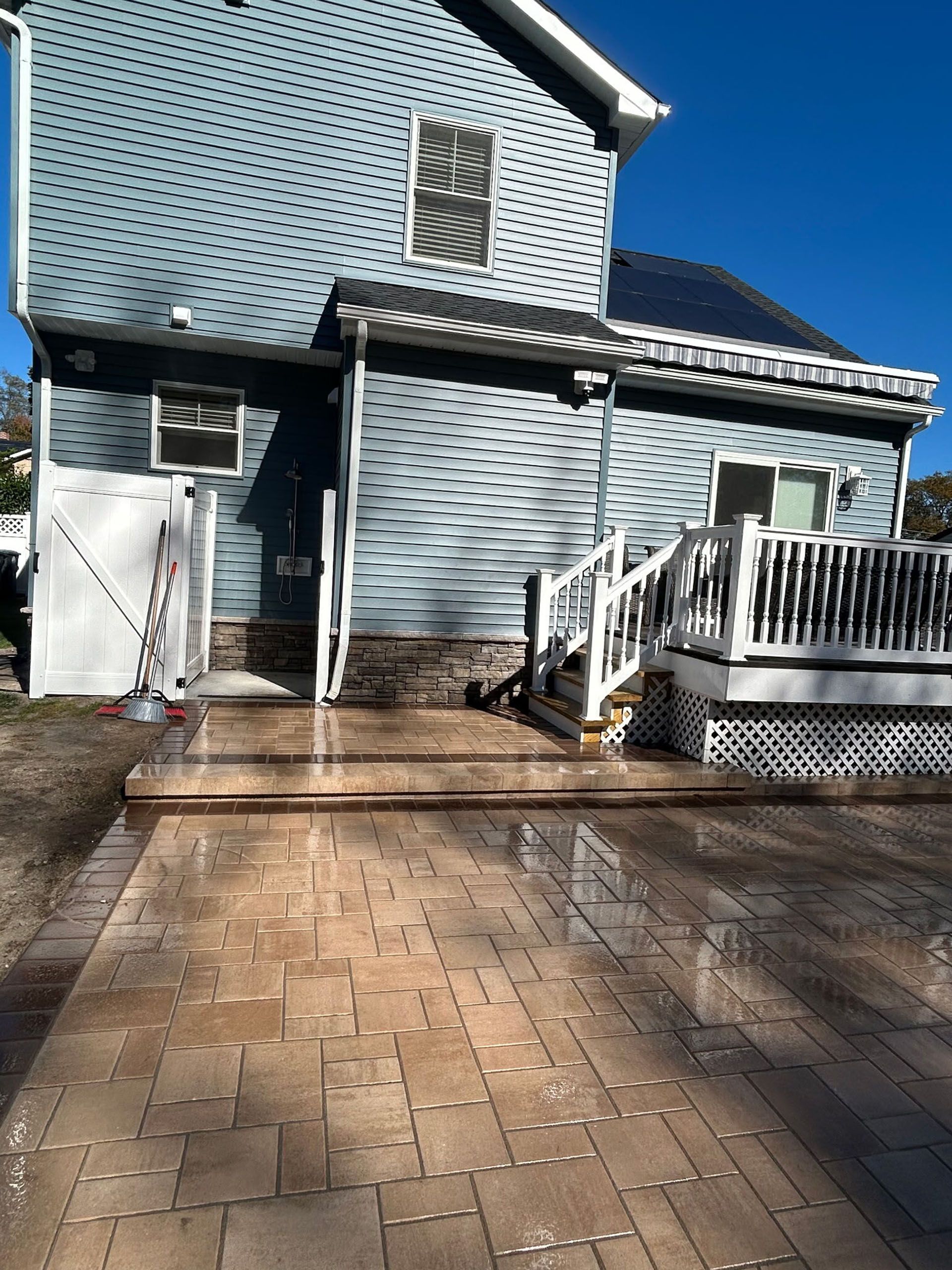 Backyard patio with stone pavers leading to a house with blue siding and a deck.