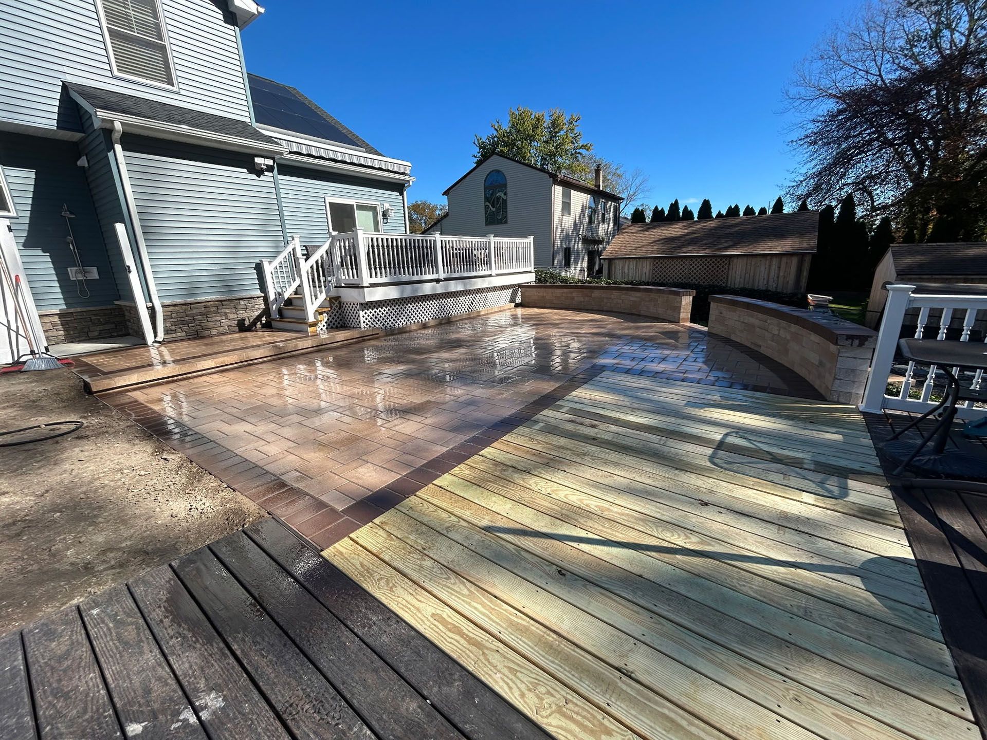 Backyard deck with newly stained wooden sections and a textured patio area.