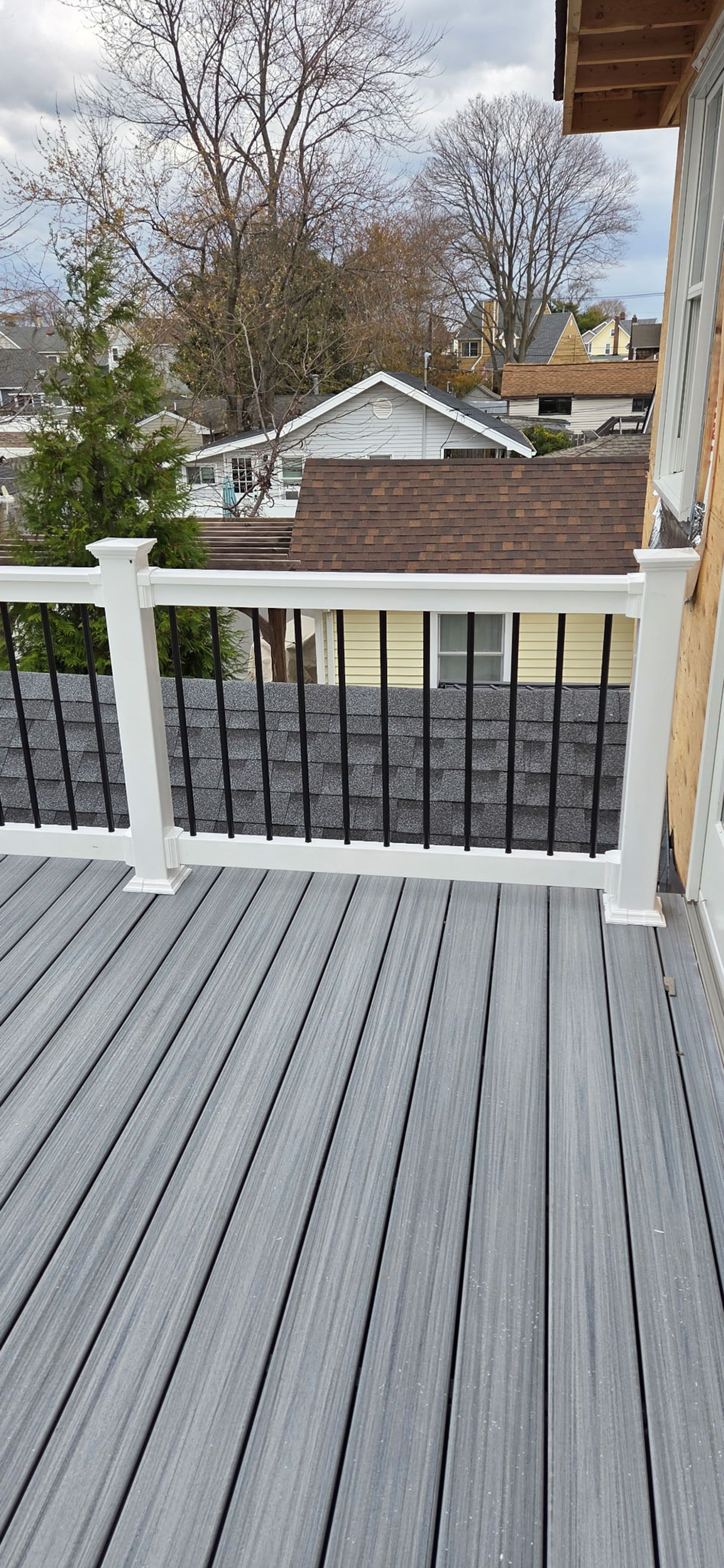 A deck with gray composite boards, white railing, and a view of houses and trees.