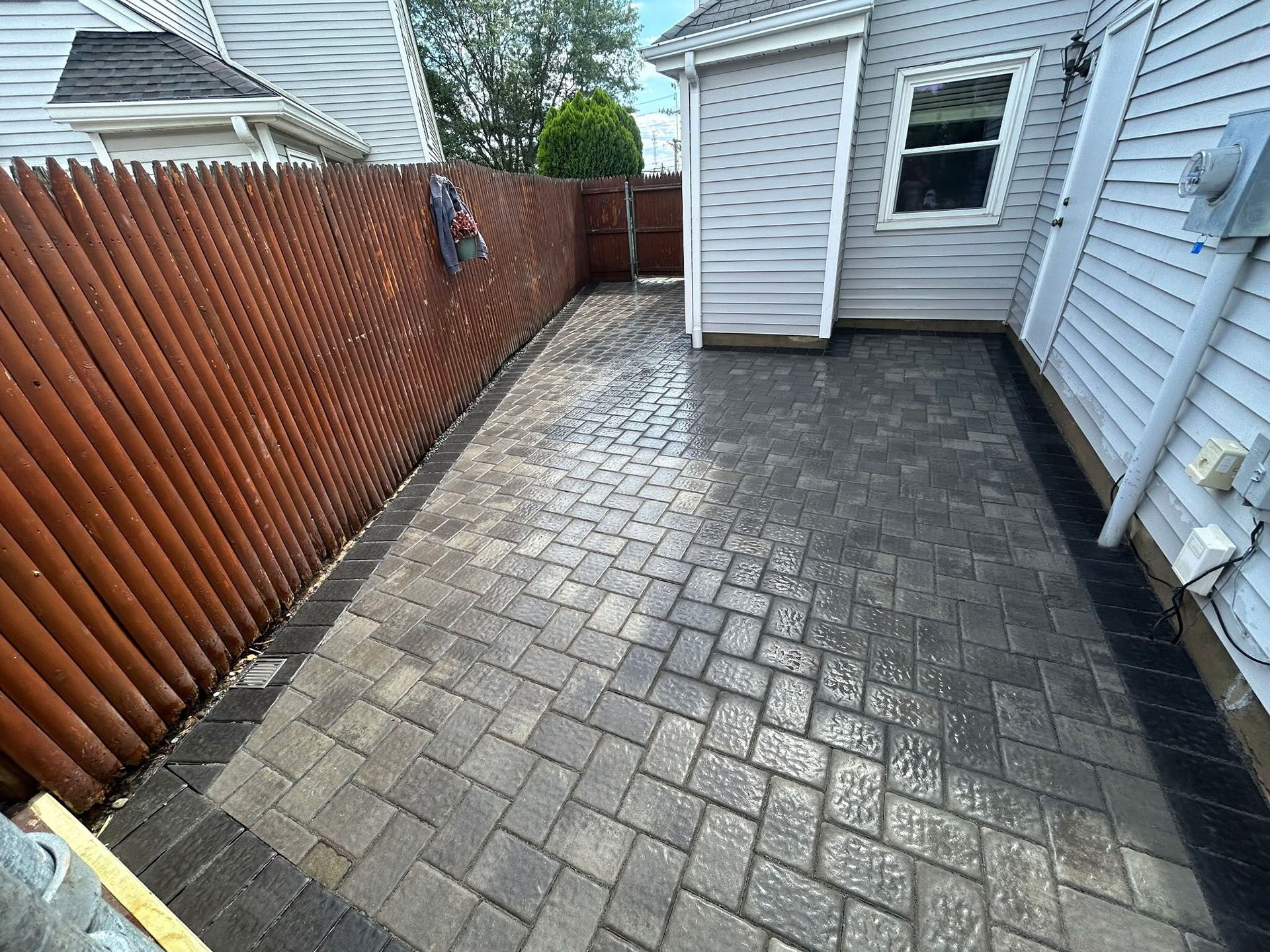 Brick patio next to a wooden fence and a light-colored house.