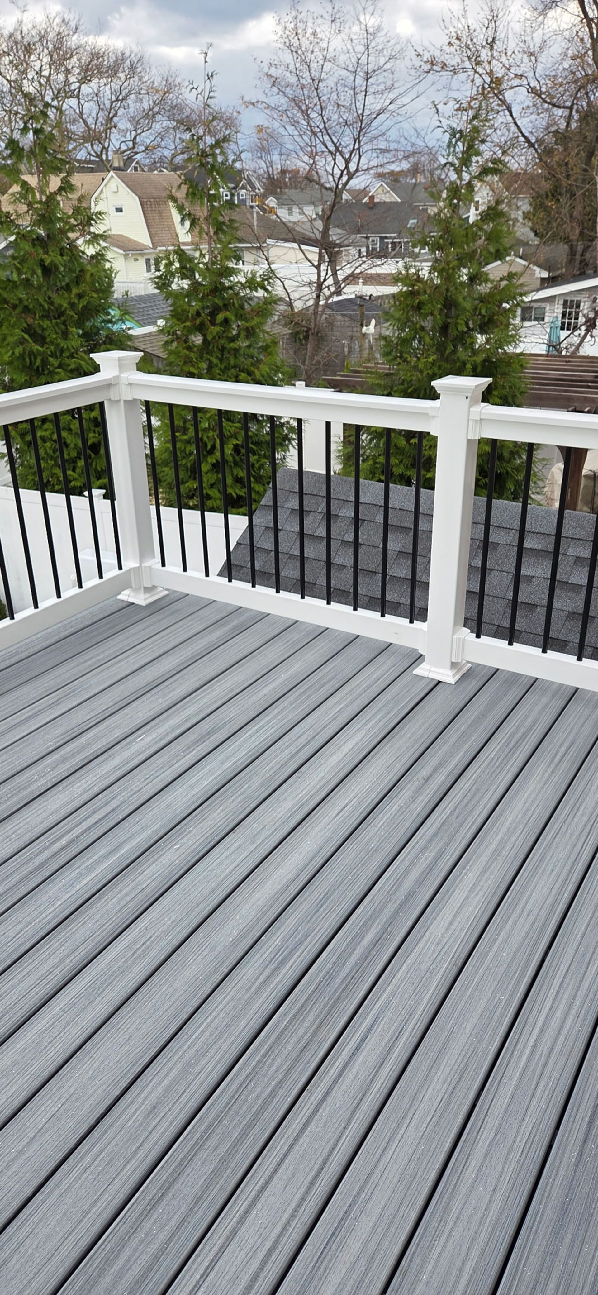 A gray deck with white railing, and black spindles overlooks a snow-covered mountain and evergreen trees.