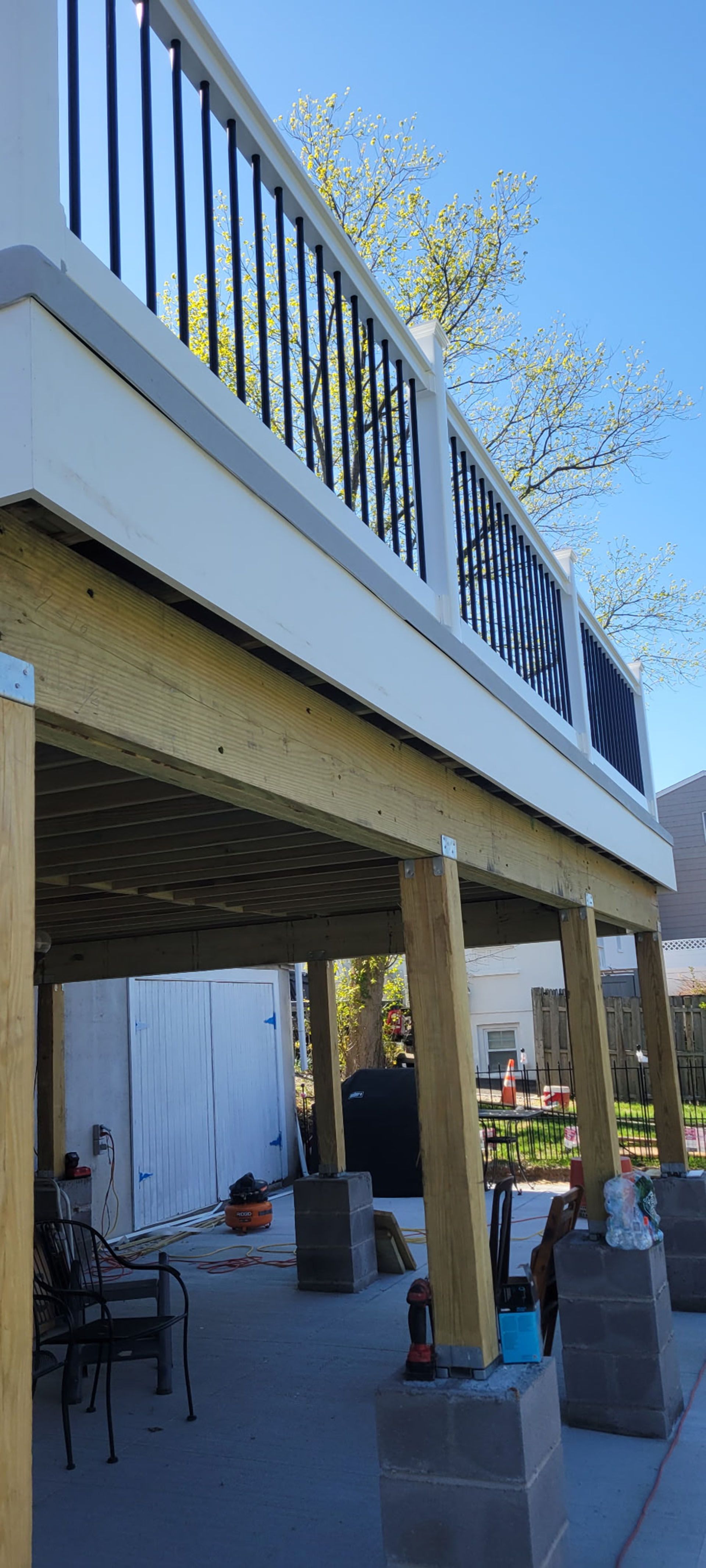 Deck under construction, supported by wooden posts on concrete blocks, with a blue sky background.