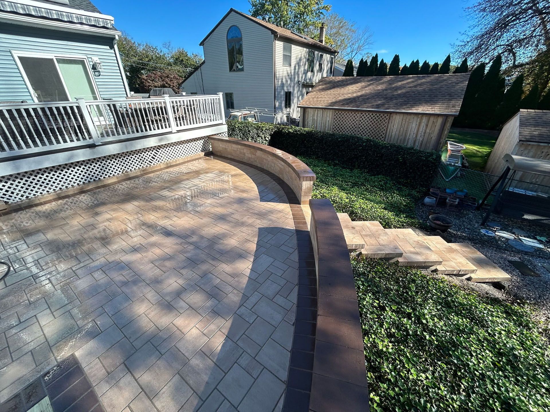 Brick patio with curved wall, steps, adjacent deck, and house in background.