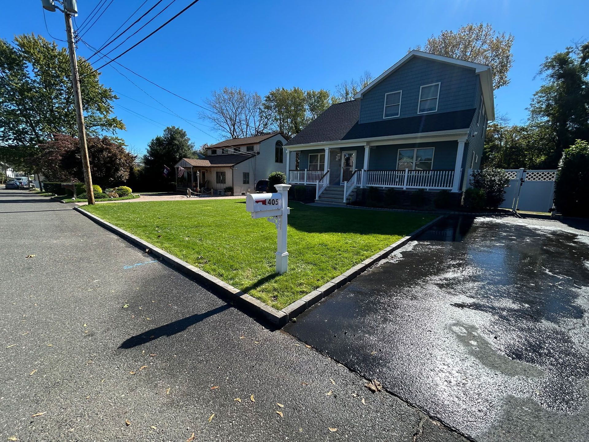 Blue house with porch, lawn, and mailbox on a sunny day. Asphalt driveway and street.