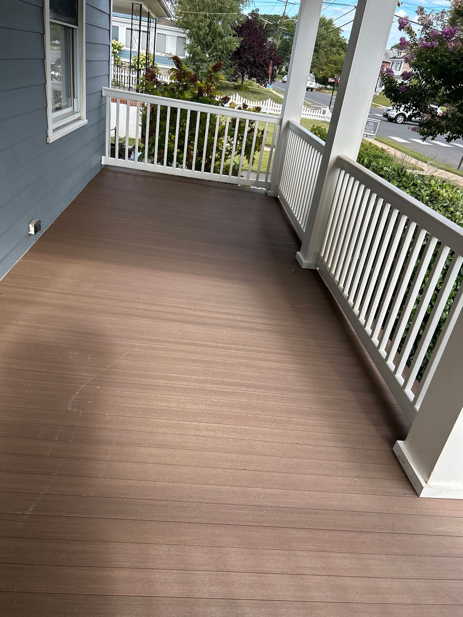 Brown wooden porch with white railing on a blue house.