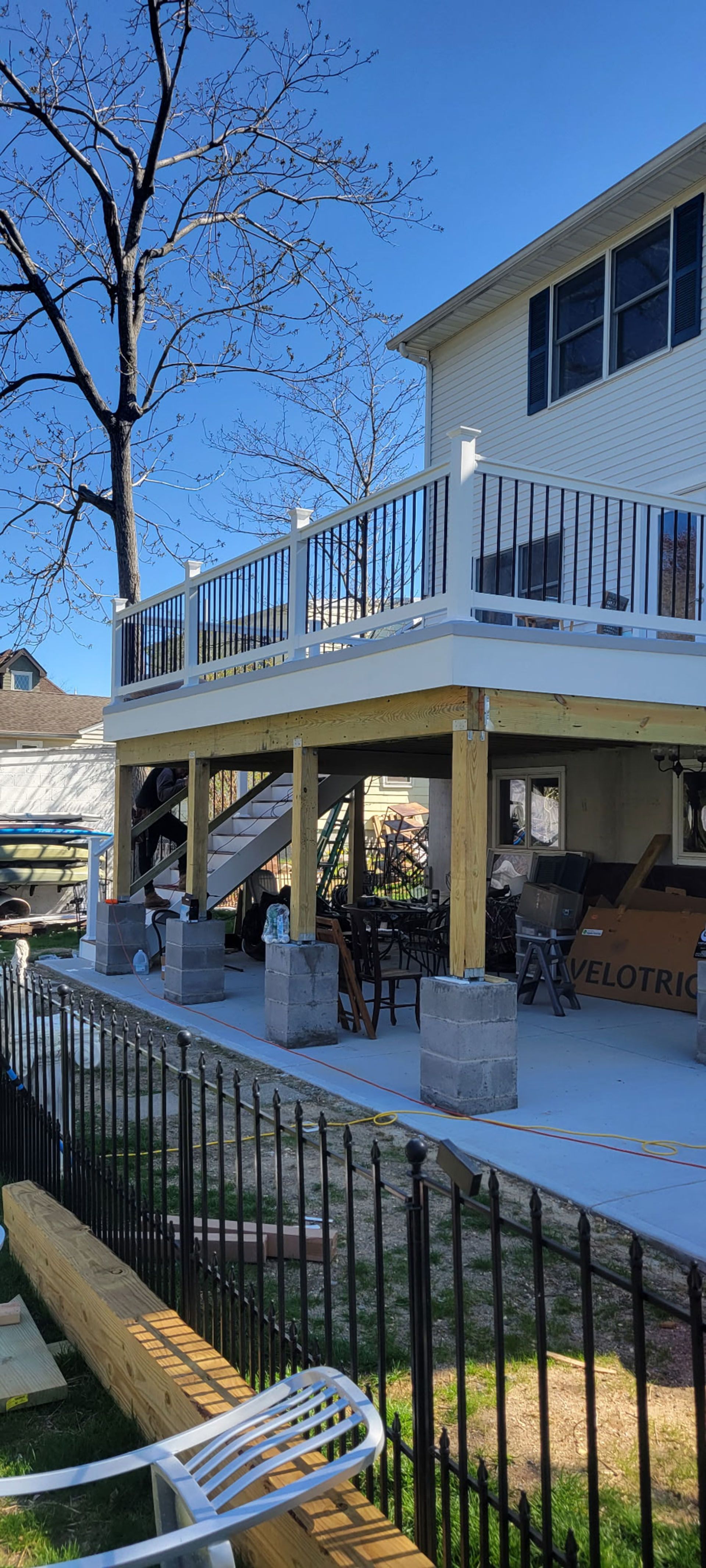Two-story house with a wooden deck and a black fence by the water.