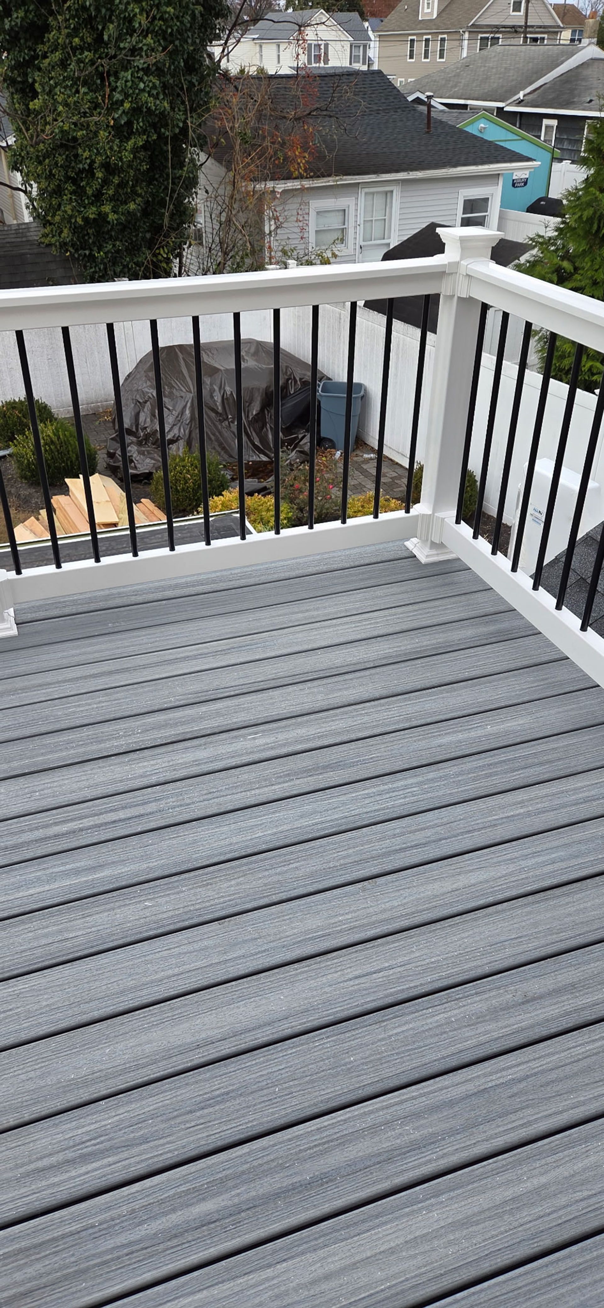 Gray composite deck with white railing and black spindles, overlooking a neighborhood.