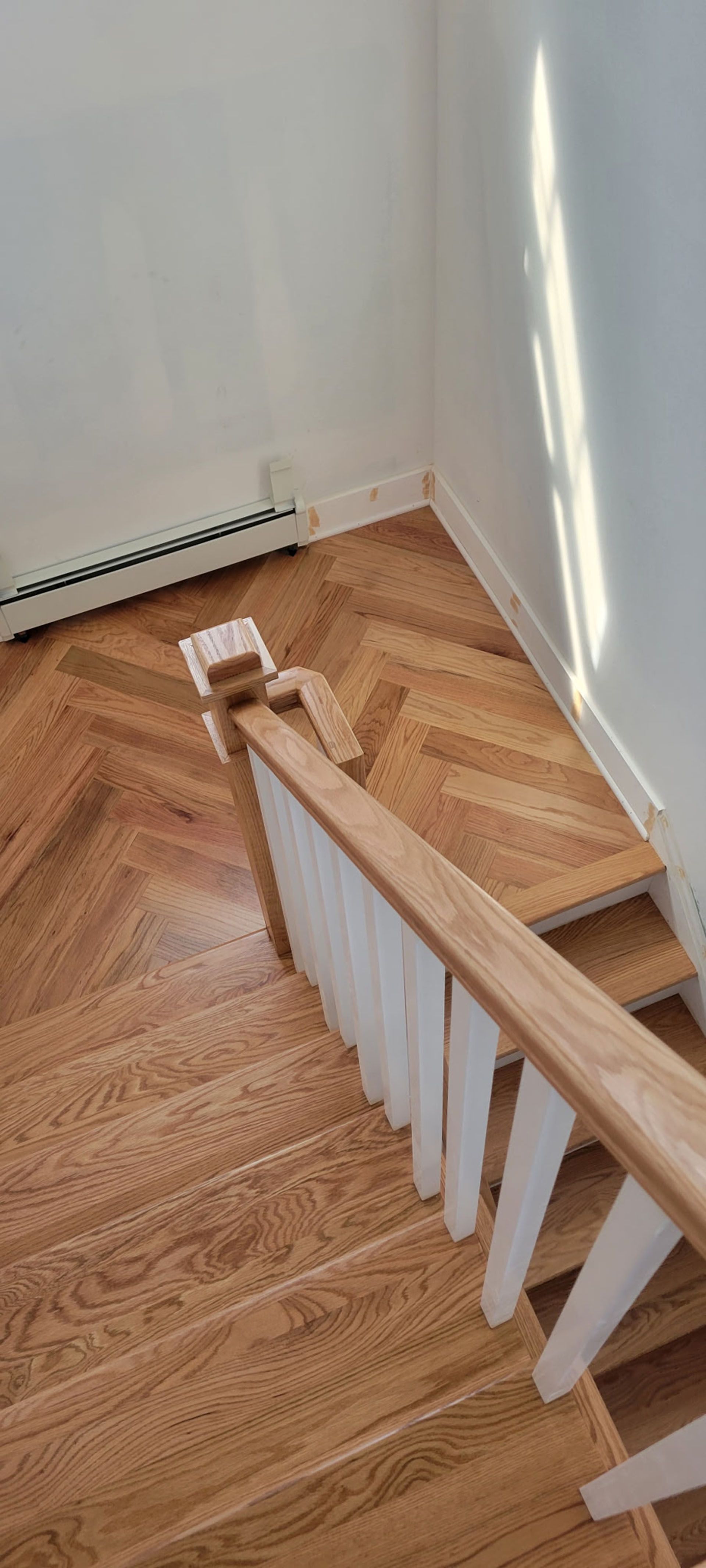 Wooden staircase with a white railing, leading down to a wood floor with a herringbone pattern.