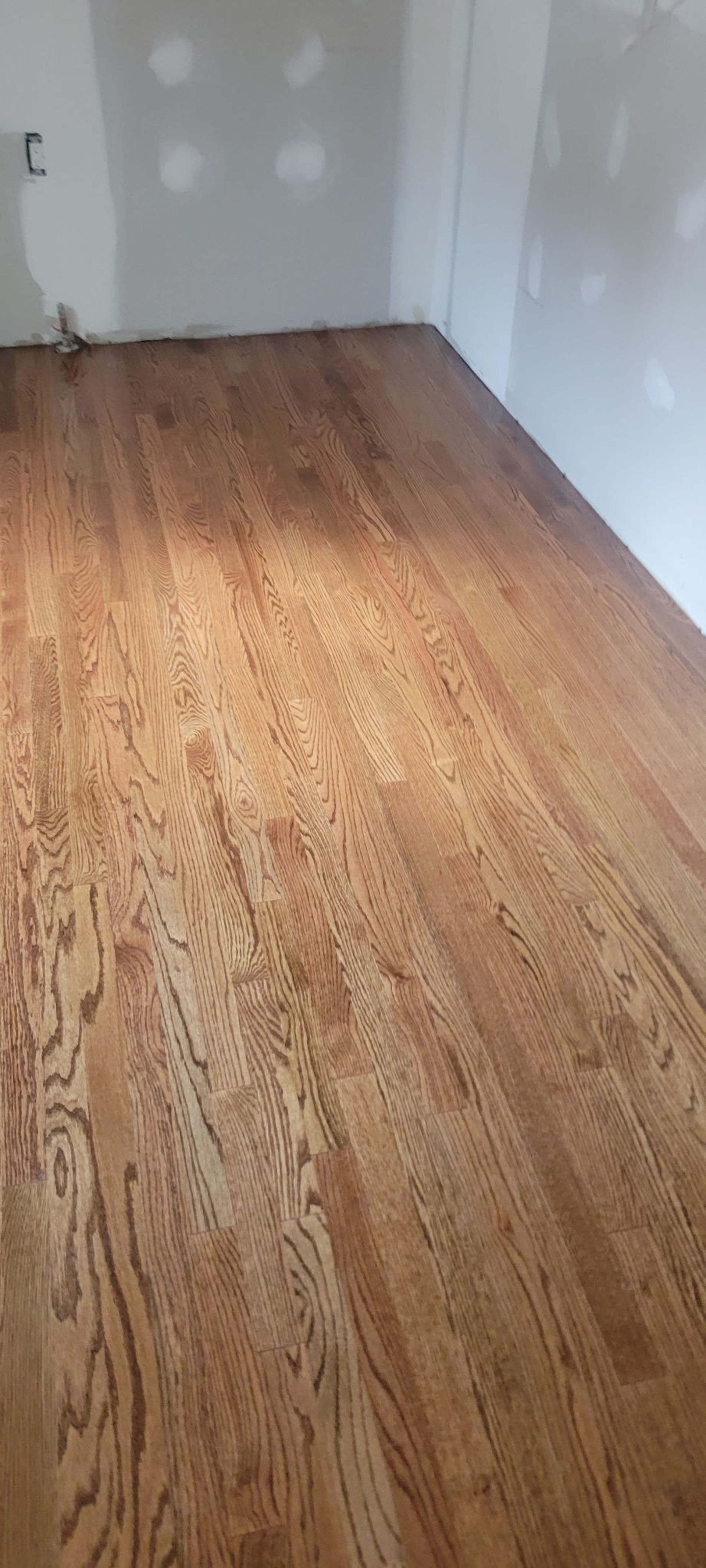 Hardwood floor in room with unfinished drywall walls.