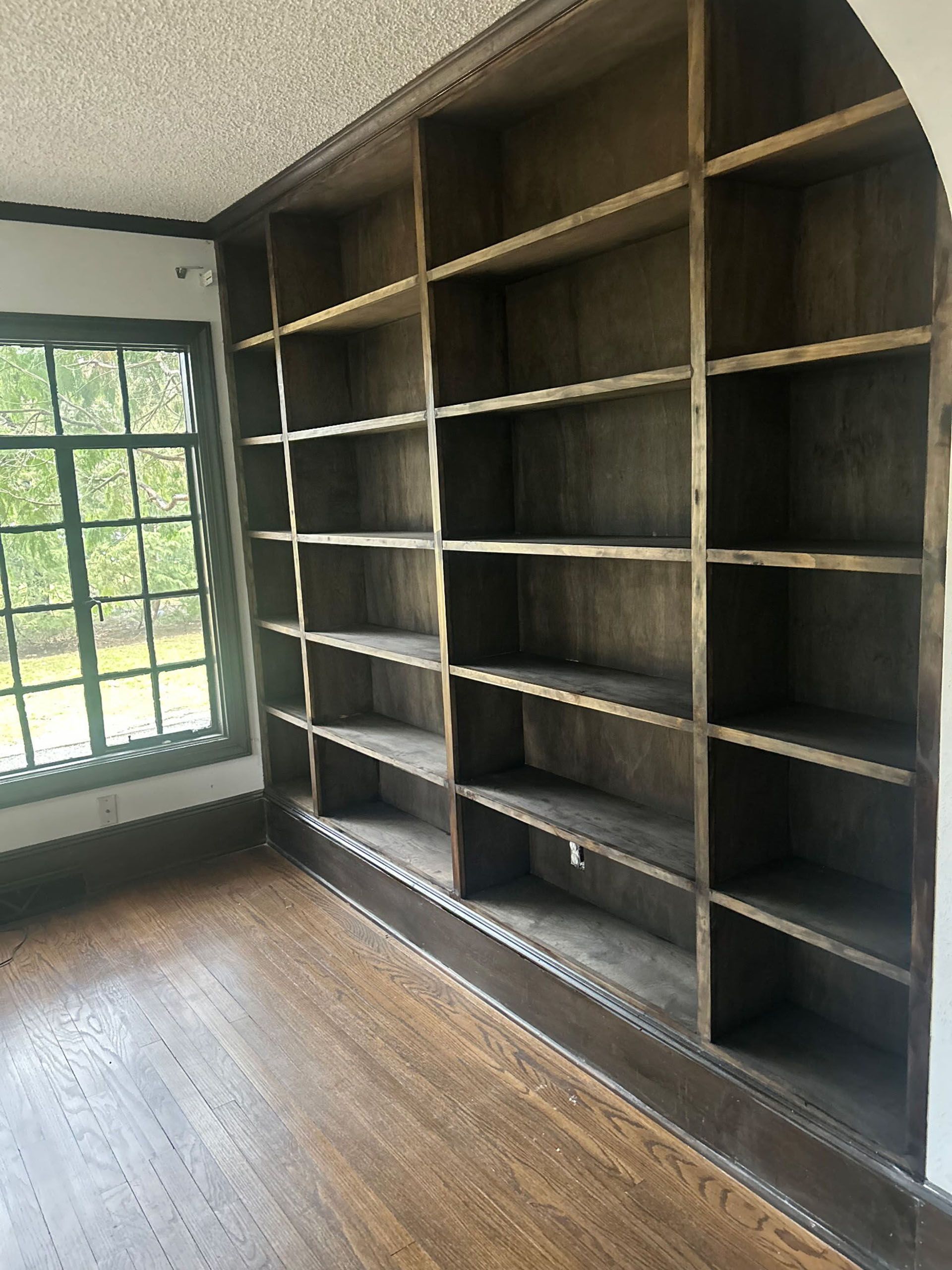Built-in wooden bookshelves against a wall, next to a window with a view.
