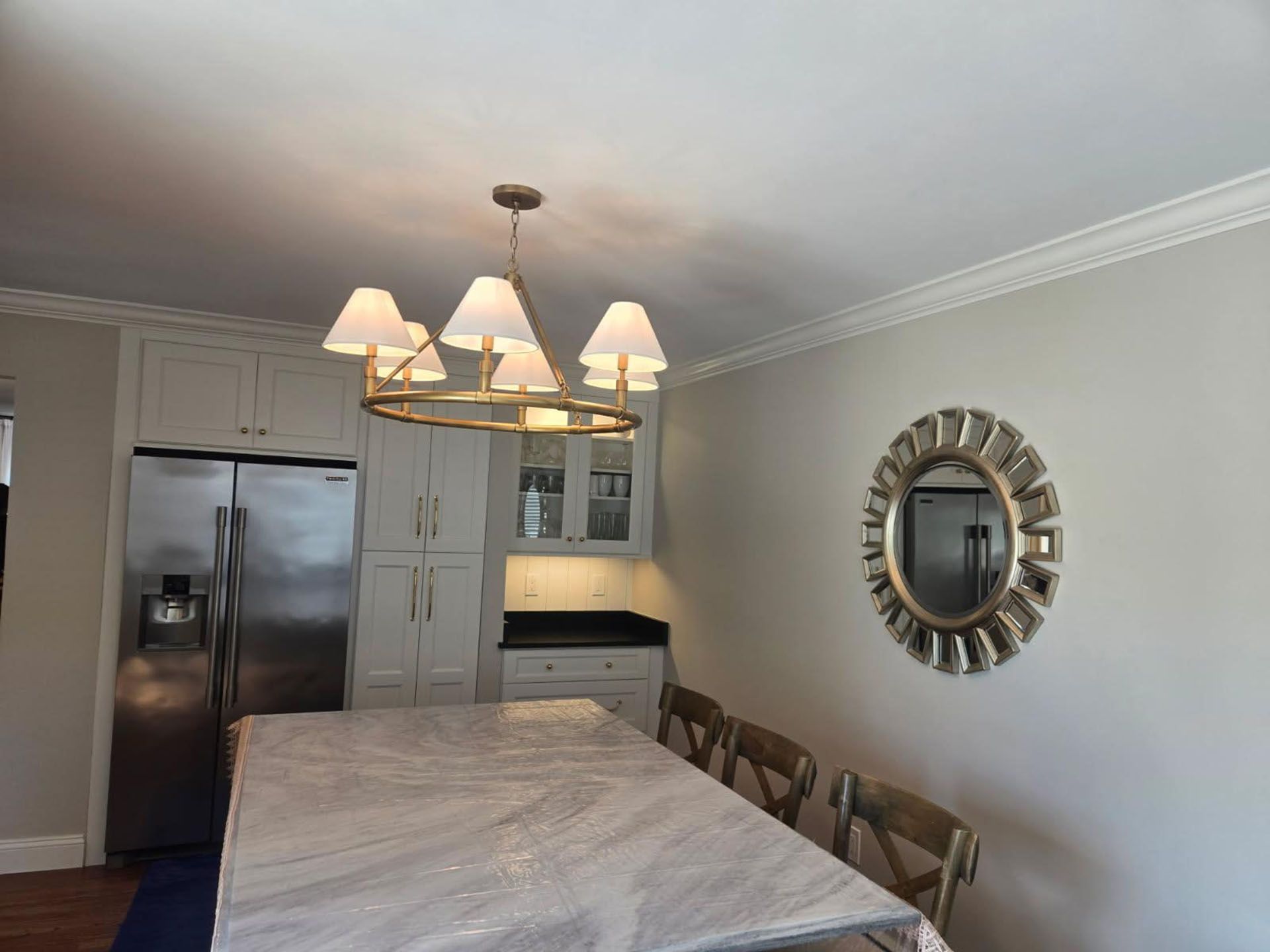 Kitchen with white cabinets, stainless steel fridge, dining table, chandelier, and a decorative mirror.