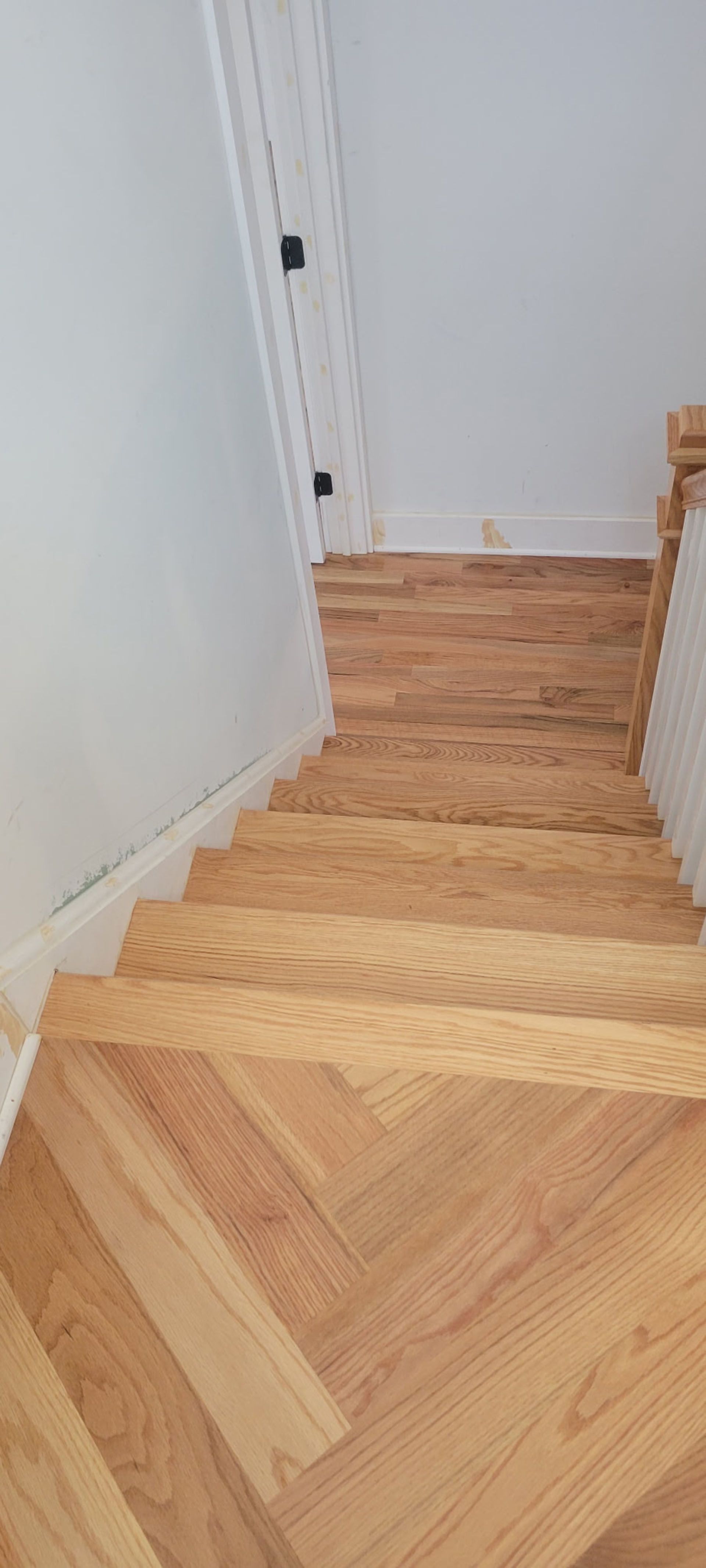 Wooden staircase with herringbone pattern, leading downwards from a white wall.
