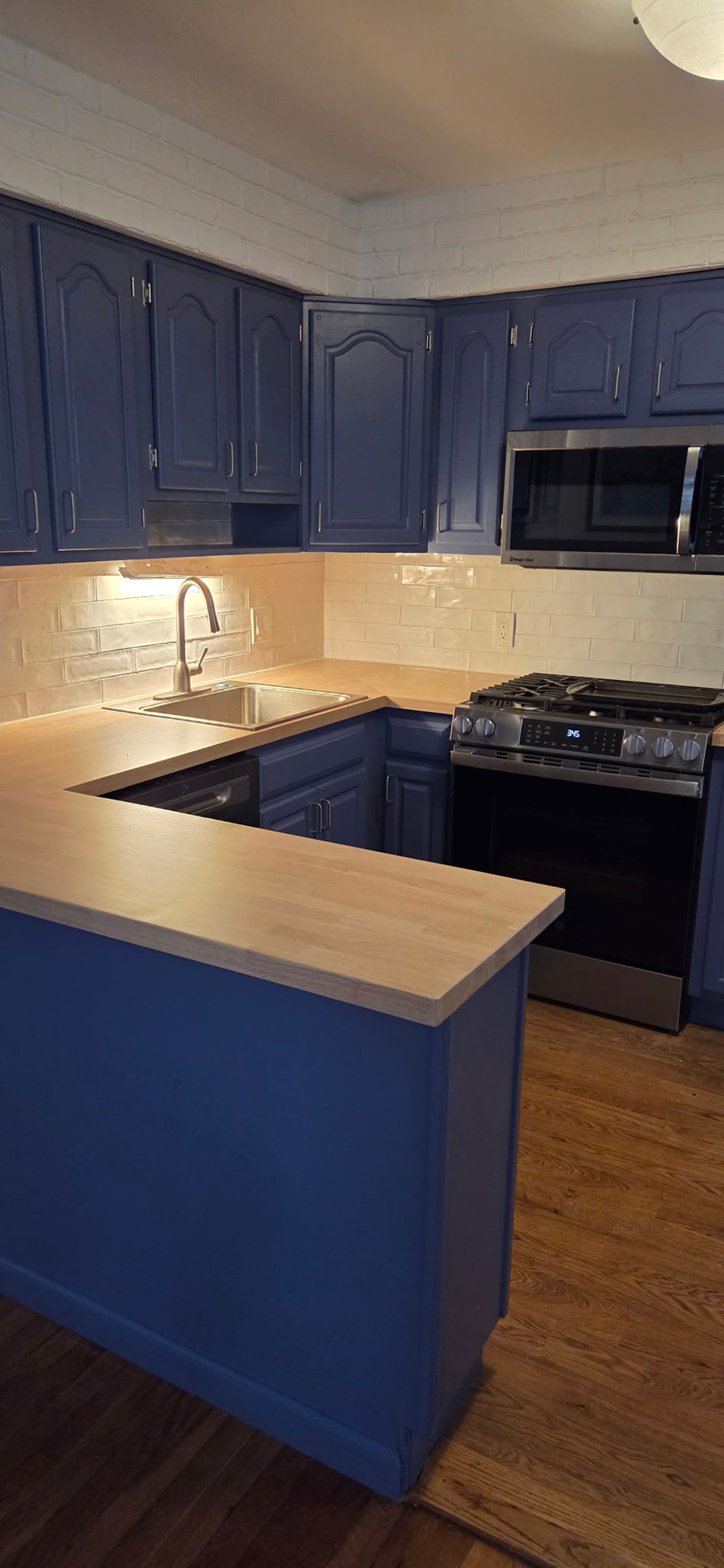 Kitchen with blue cabinets, light wood counters, and a stainless steel stove and microwave.