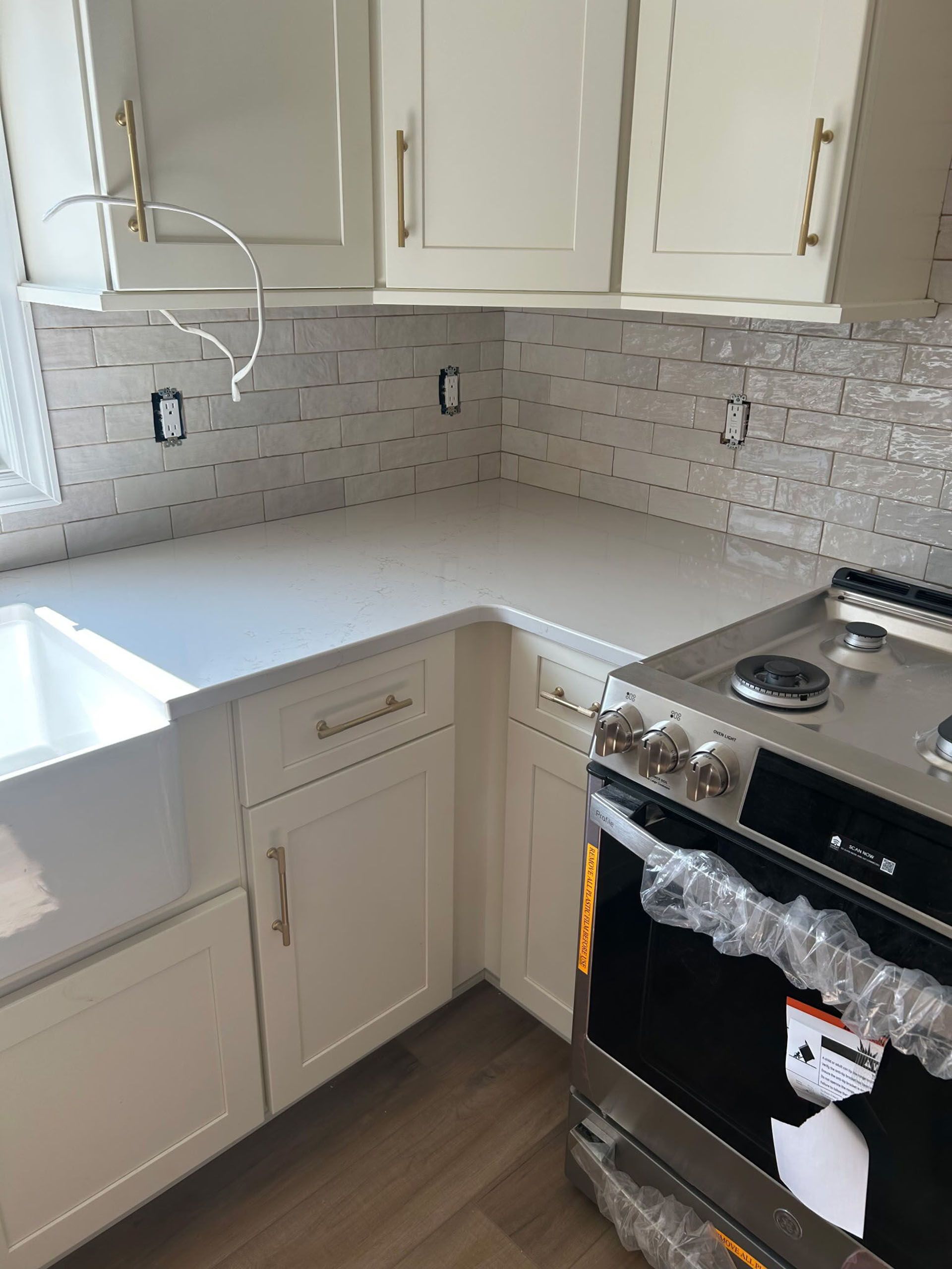 White kitchen cabinets, countertop, and backsplash. Stainless steel oven with clear wrap.
