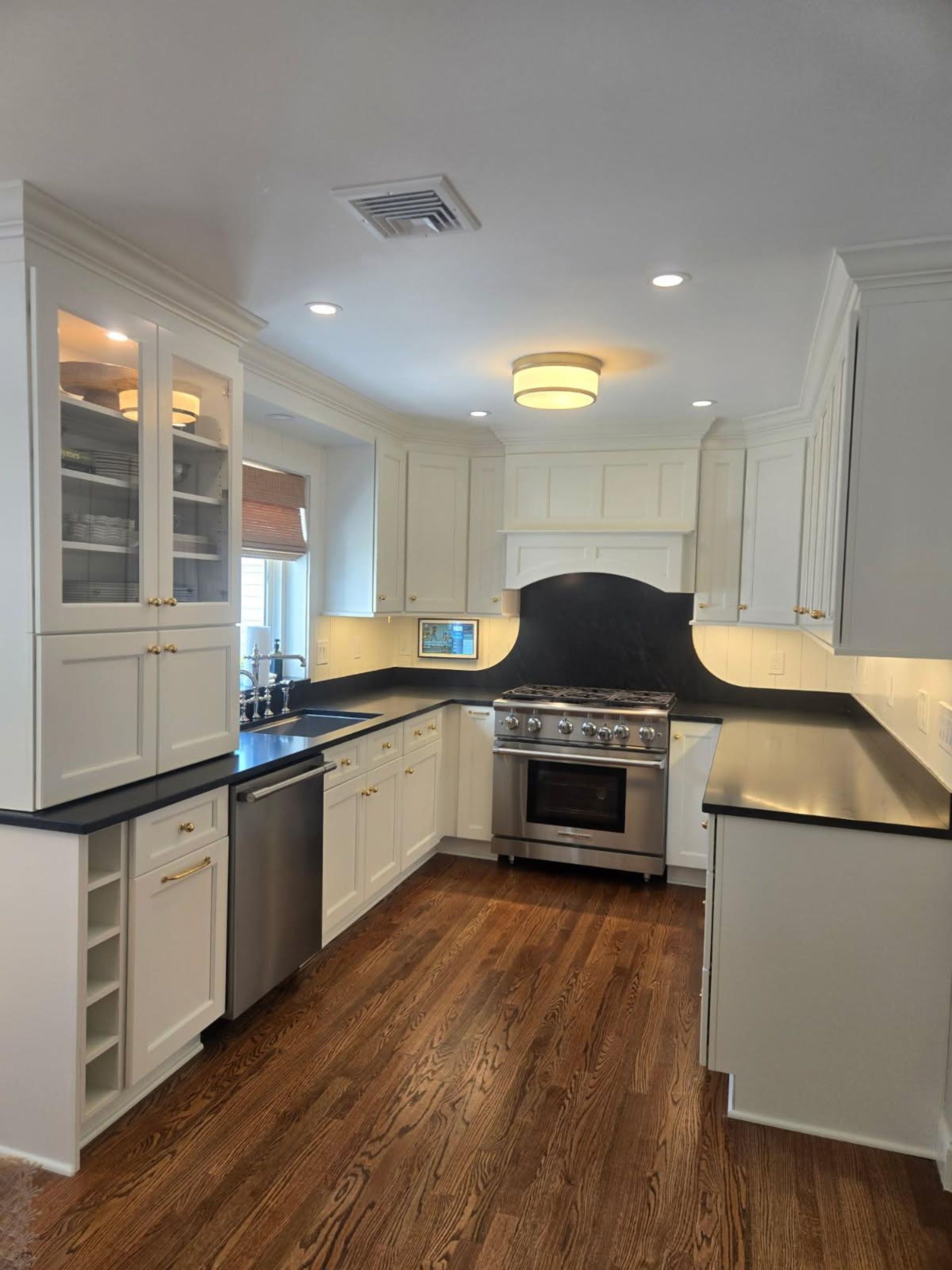 White kitchen with stainless steel appliances, dark countertops, and hardwood floors.