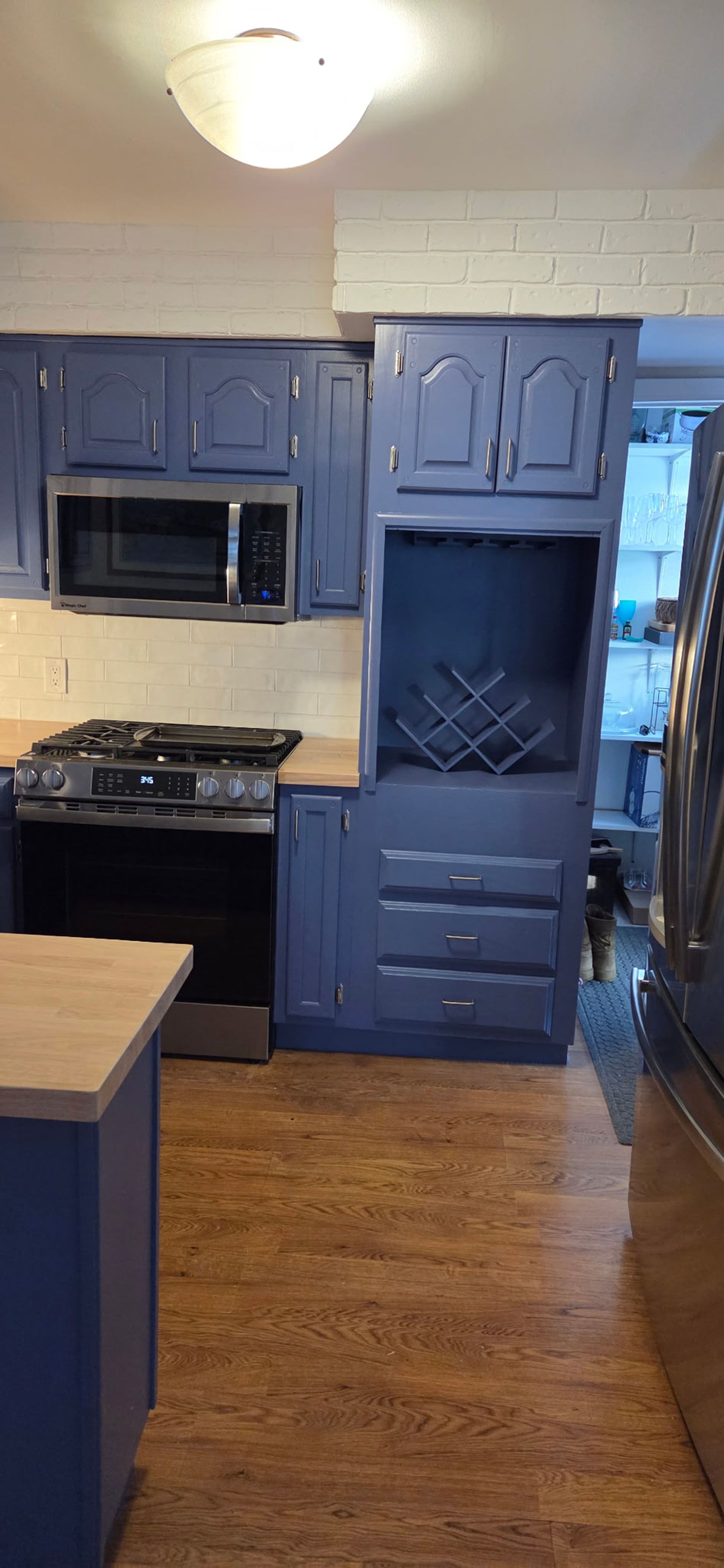 A kitchen with blue cabinets, a microwave, a stove, and wood-look flooring.