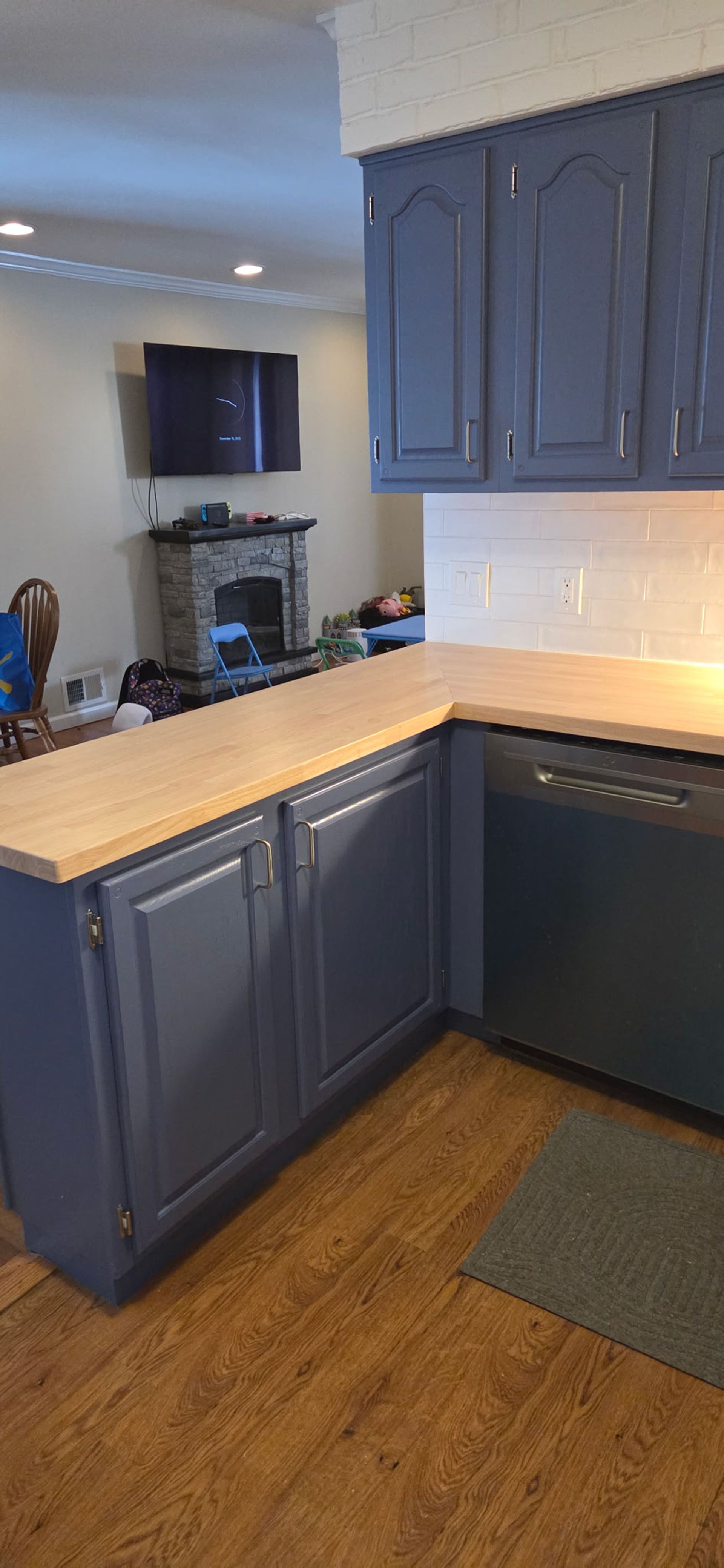 A kitchen with blue cabinets, a light countertop, and a wooden floor. A person is visible in the background.
