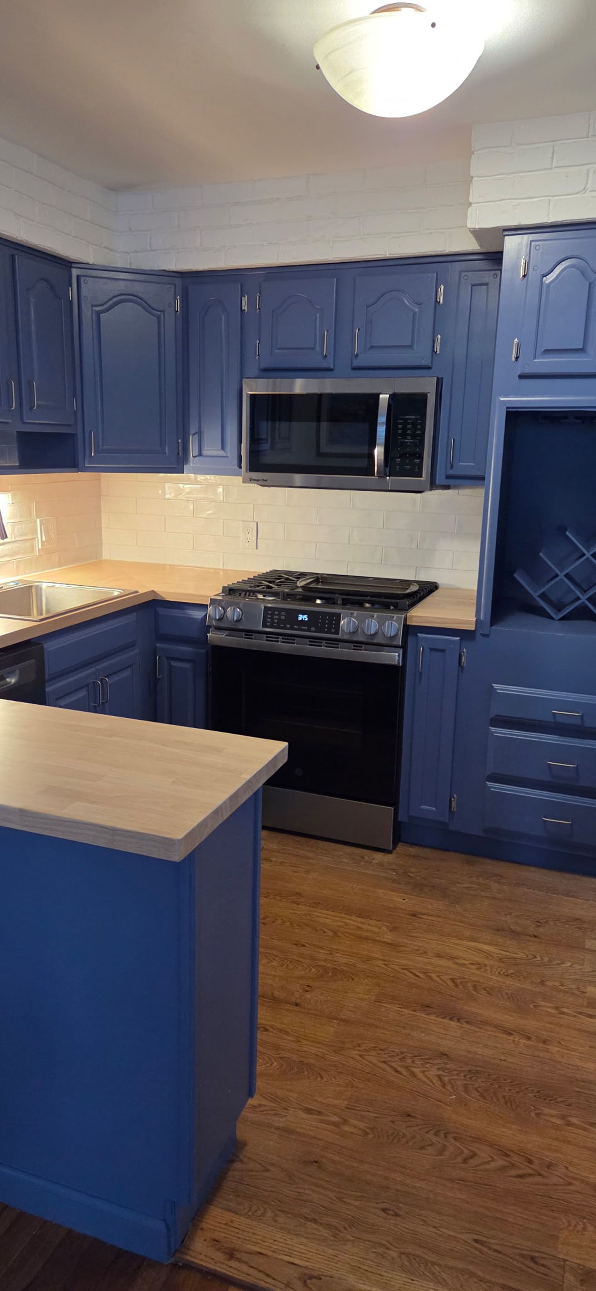Blue kitchen with wooden floor and beige countertops. A stainless steel microwave and stove are visible.