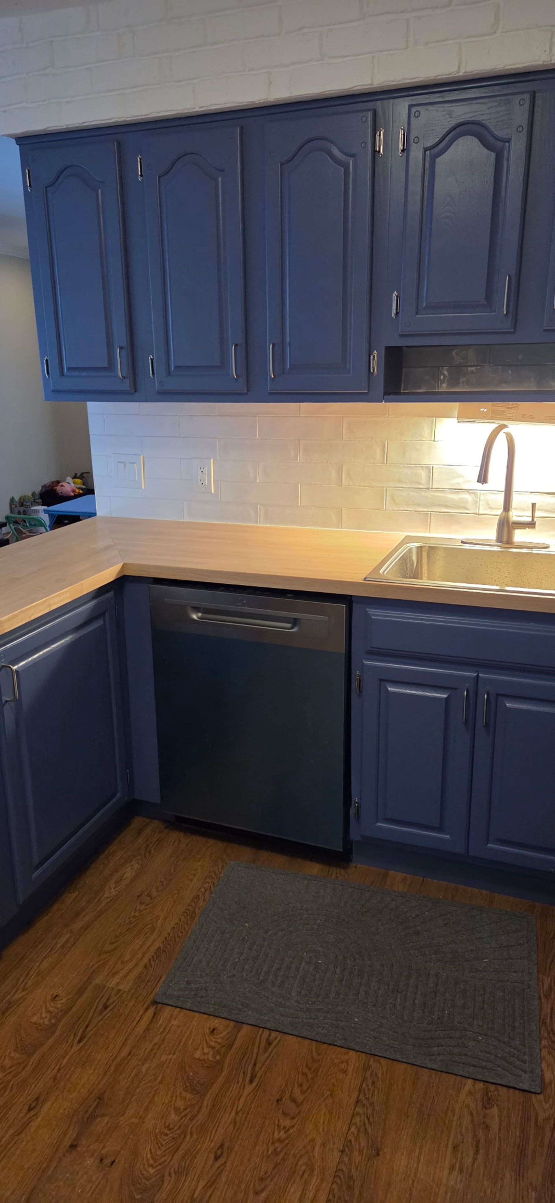 Kitchen with navy blue cabinets, light backsplash, and brown countertops; a dishwasher and sink are visible.