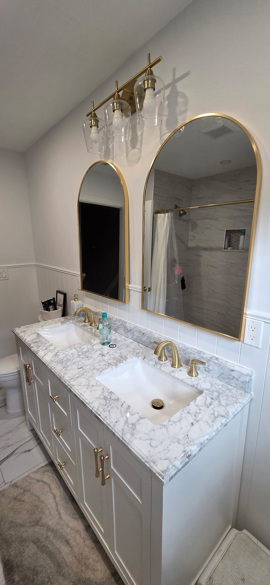 A modern bathroom with a white vanity, marble countertop, arch mirrors, and gold accents.