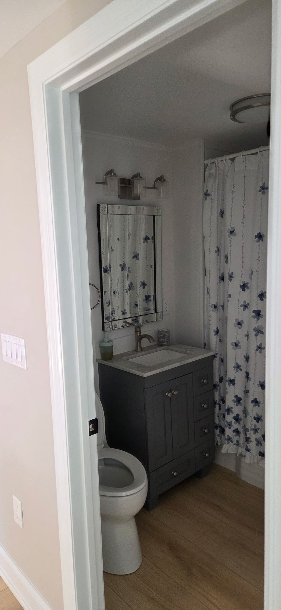 Bathroom interior with a gray vanity, a toilet, and a shower with a patterned curtain.