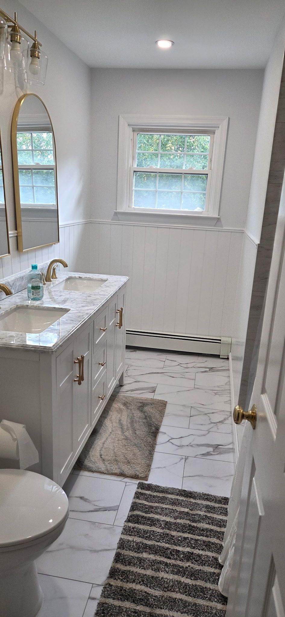 White bathroom with a double vanity, window, and marble tile floor.