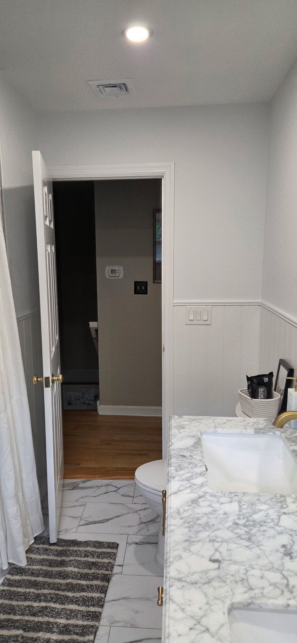 Bathroom with an open door, showing a sink, toilet, and marble-patterned flooring.