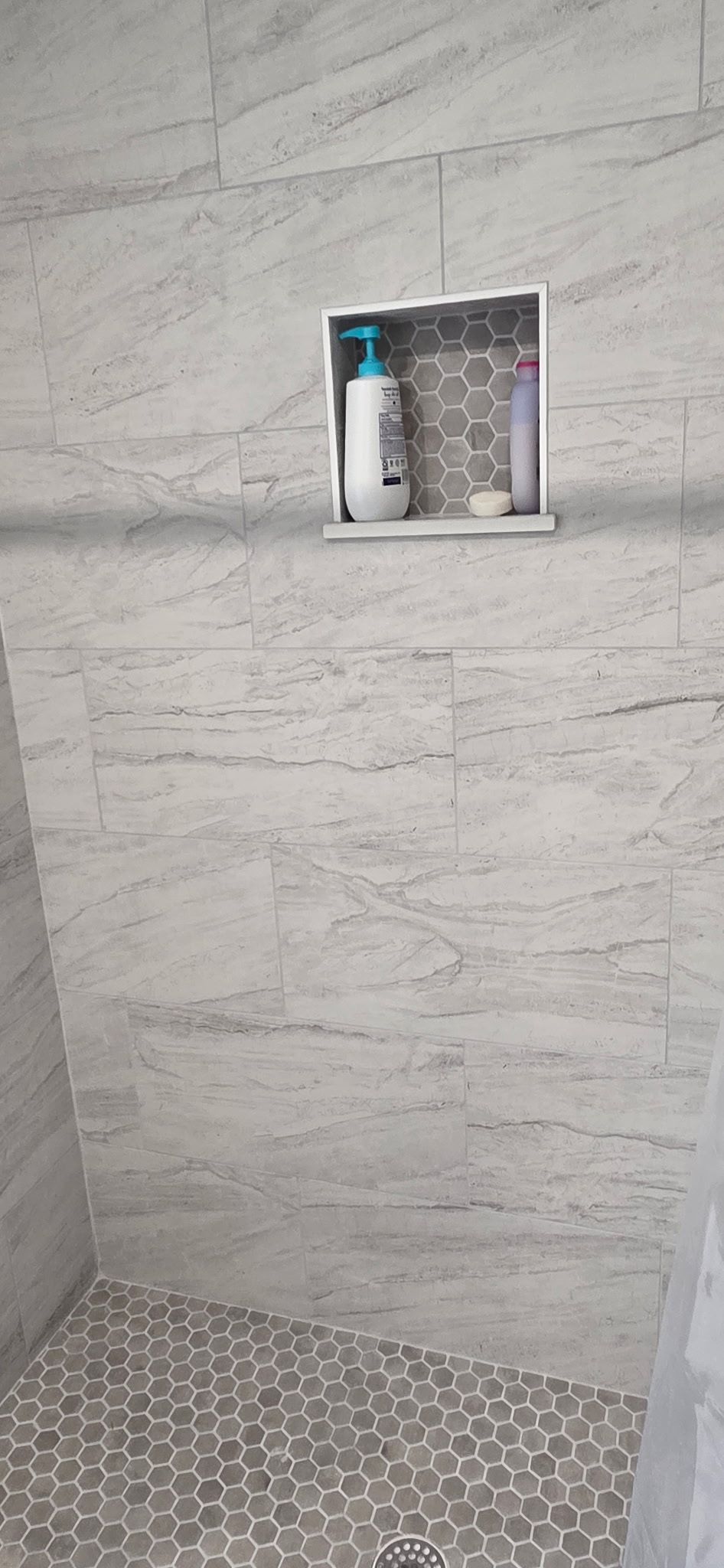 Shower with grey stone tile walls, pebble floor, and a recessed toiletries niche.