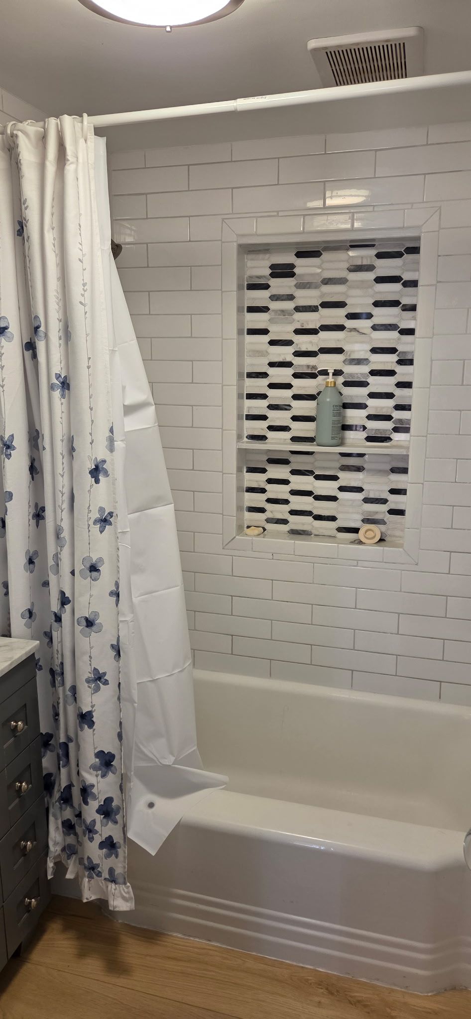 Bathroom with a white bathtub and shower with white and black tile, a blue floral shower curtain.