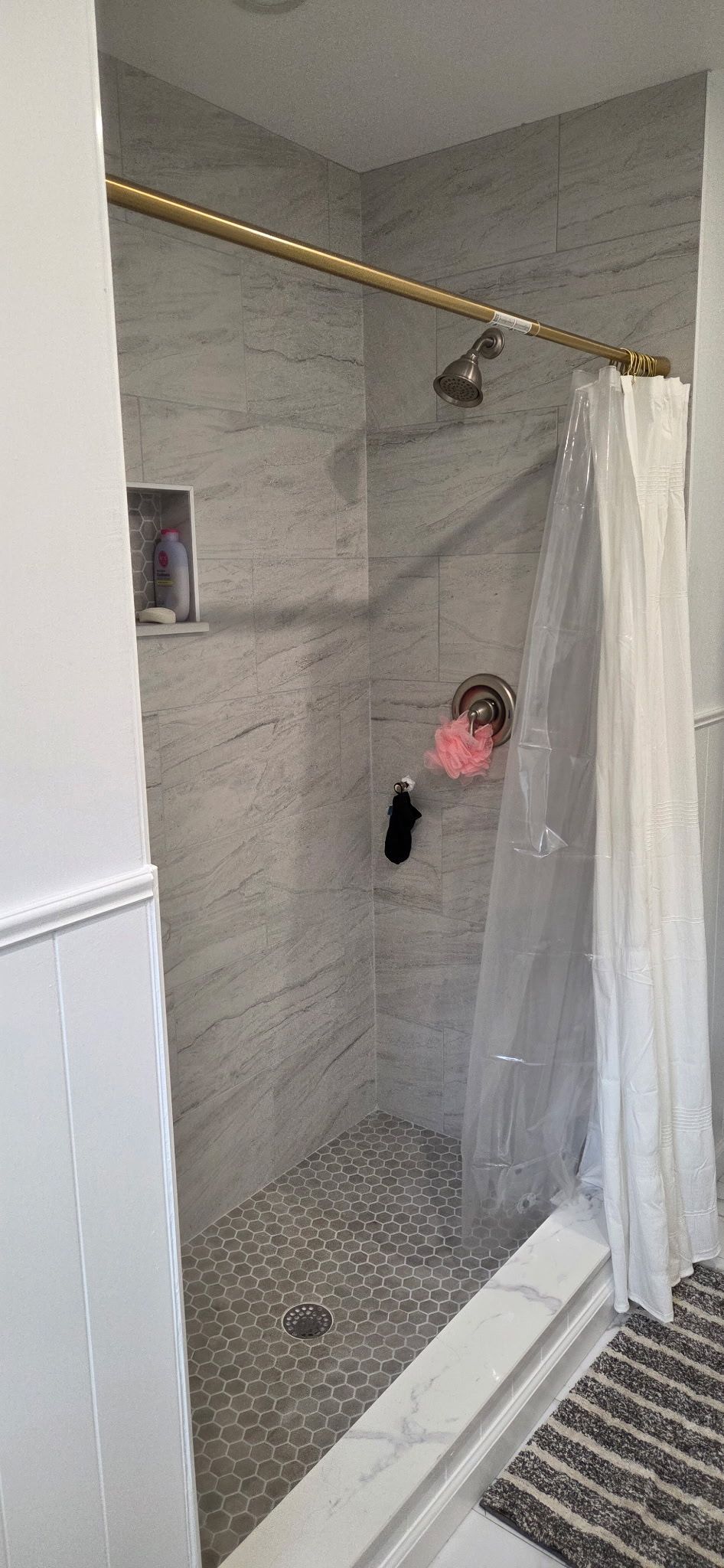 A shower with marble tile walls and pebble stone flooring. A clear shower door and gold fixtures.