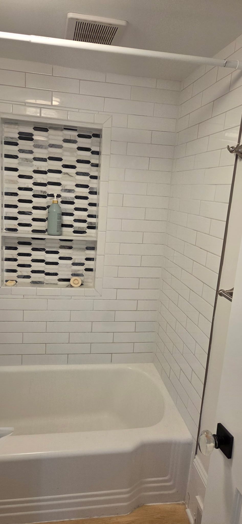 White tiled shower with a decorative mosaic niche, and a white bathtub.