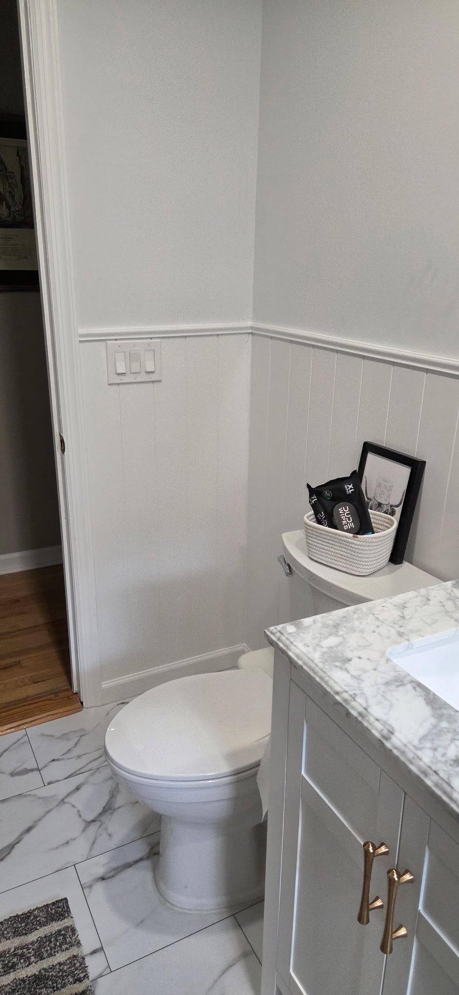 Bathroom with white walls and marble floor; toilet, sink, and decorative items.