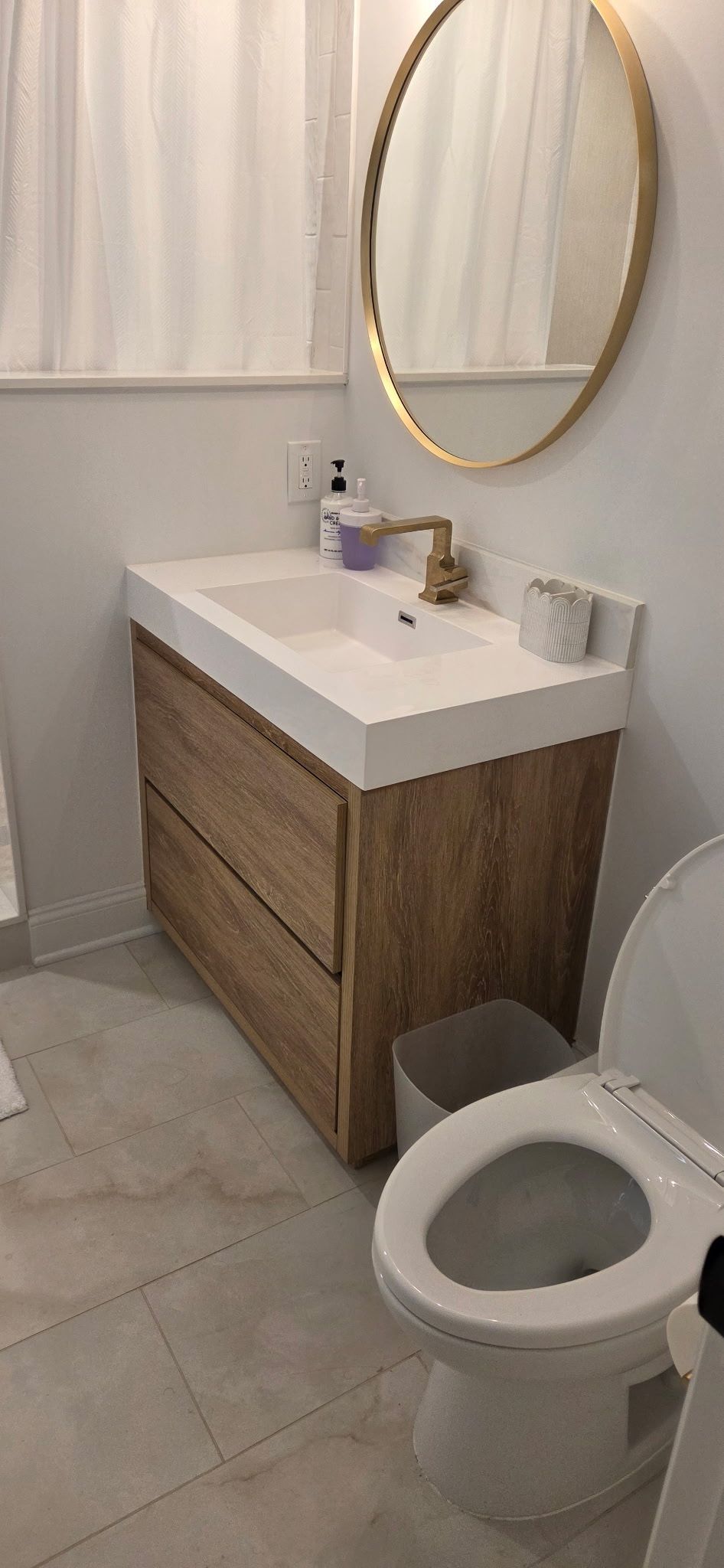 Bathroom with wooden vanity, oval mirror, and toilet.