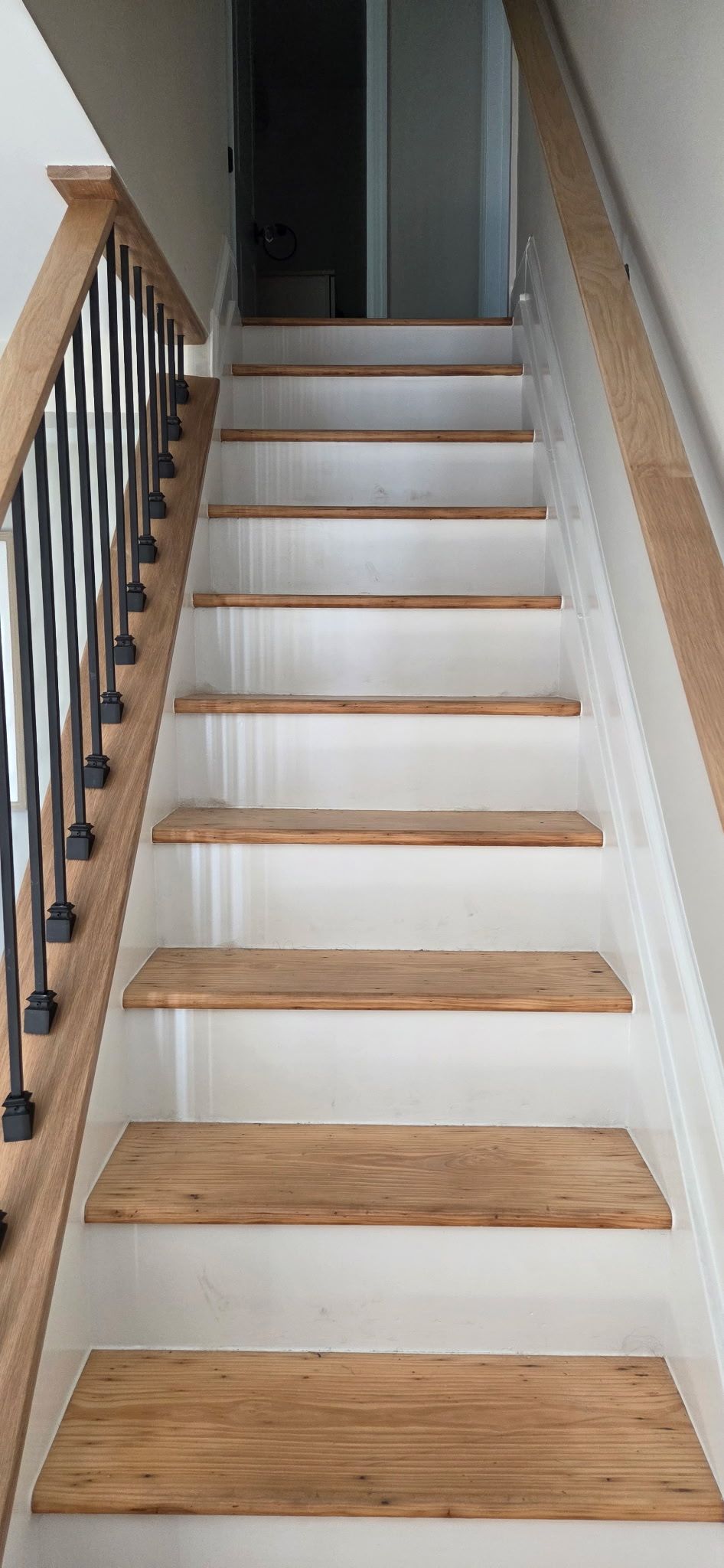 Staircase with wooden steps and a black railing on the left and a wooden handrail on the right.