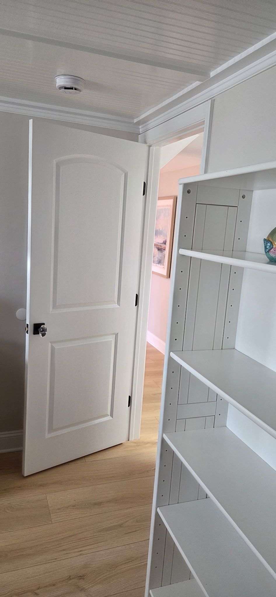 White door open into another room, with a white bookshelf visible. Light-colored carpet and ceilings.