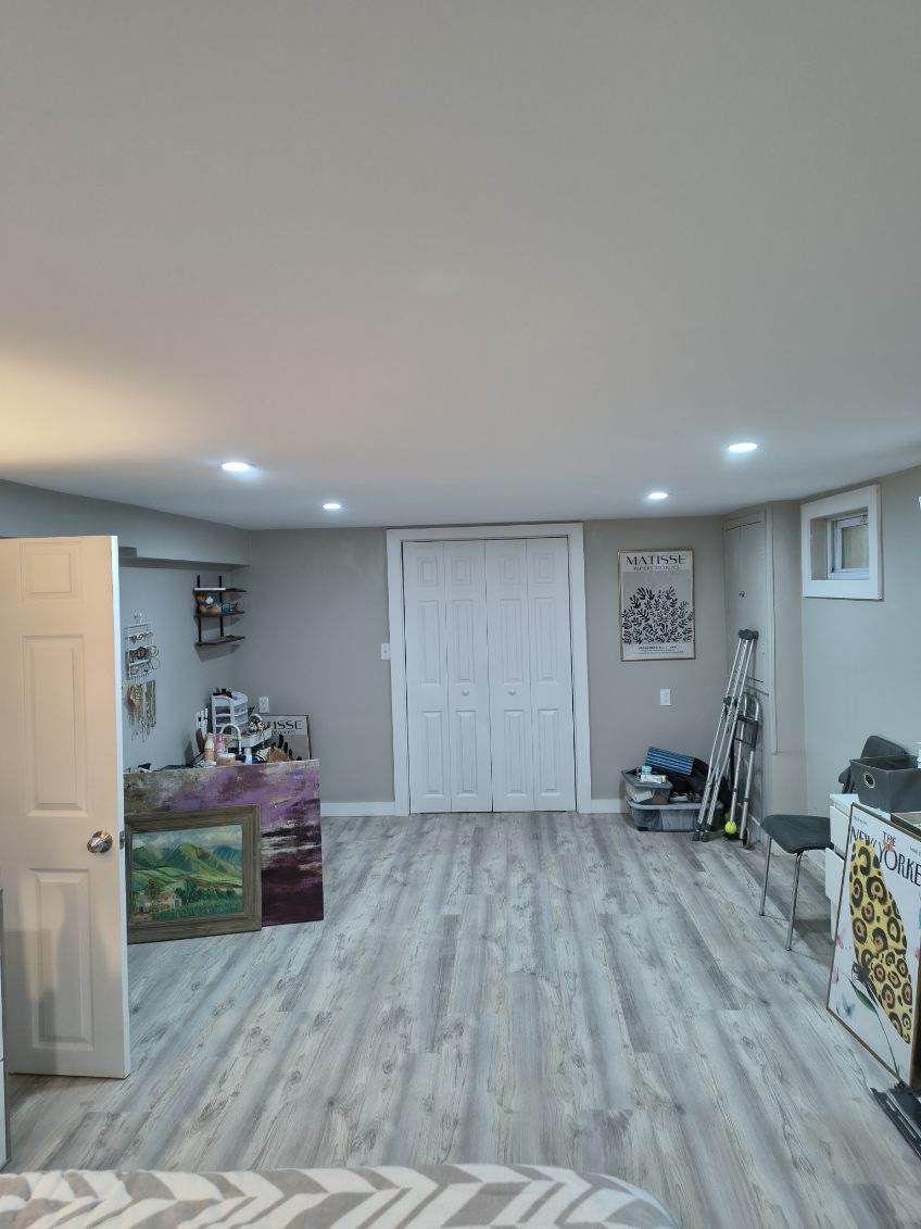 Basement room with gray walls, light wood floor, white closet doors, and art.