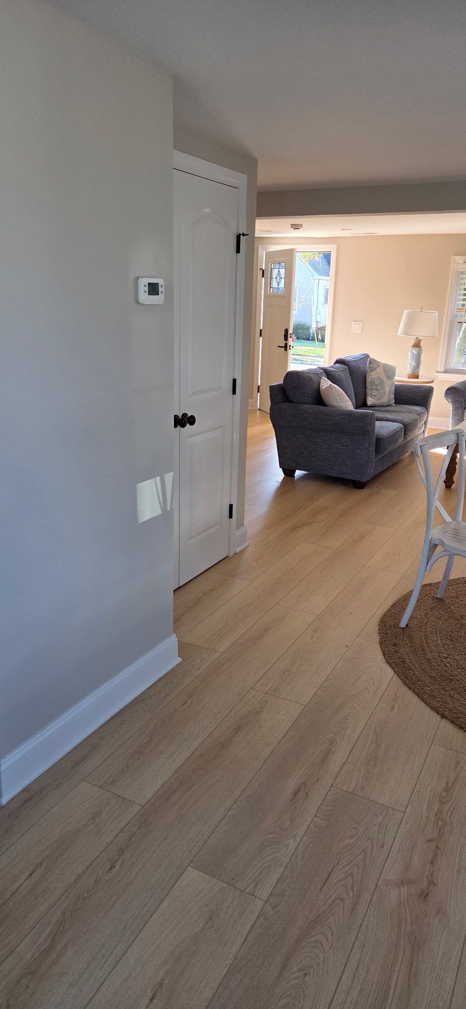 Interior view of a hallway with hardwood flooring leading to a living room with a sofa.
