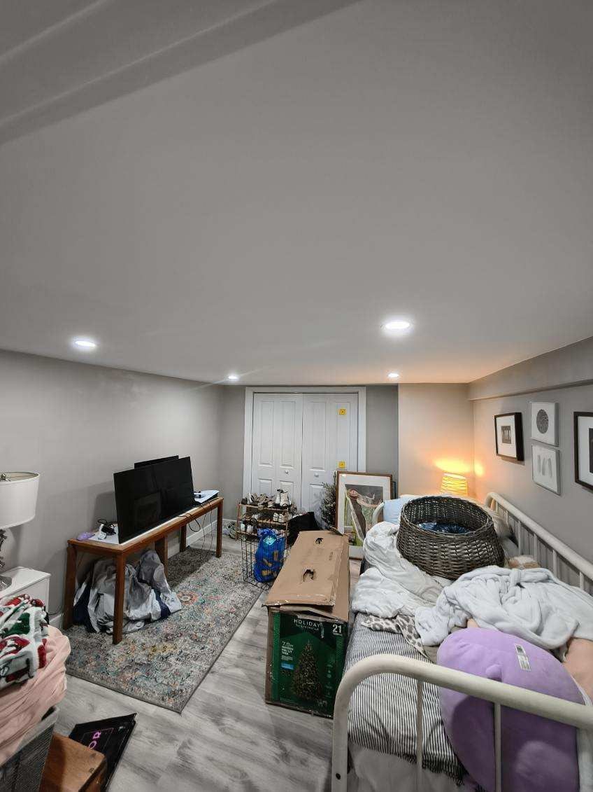 Messy bedroom with a bed, TV, and scattered items. Gray walls, white ceiling, and a rug.