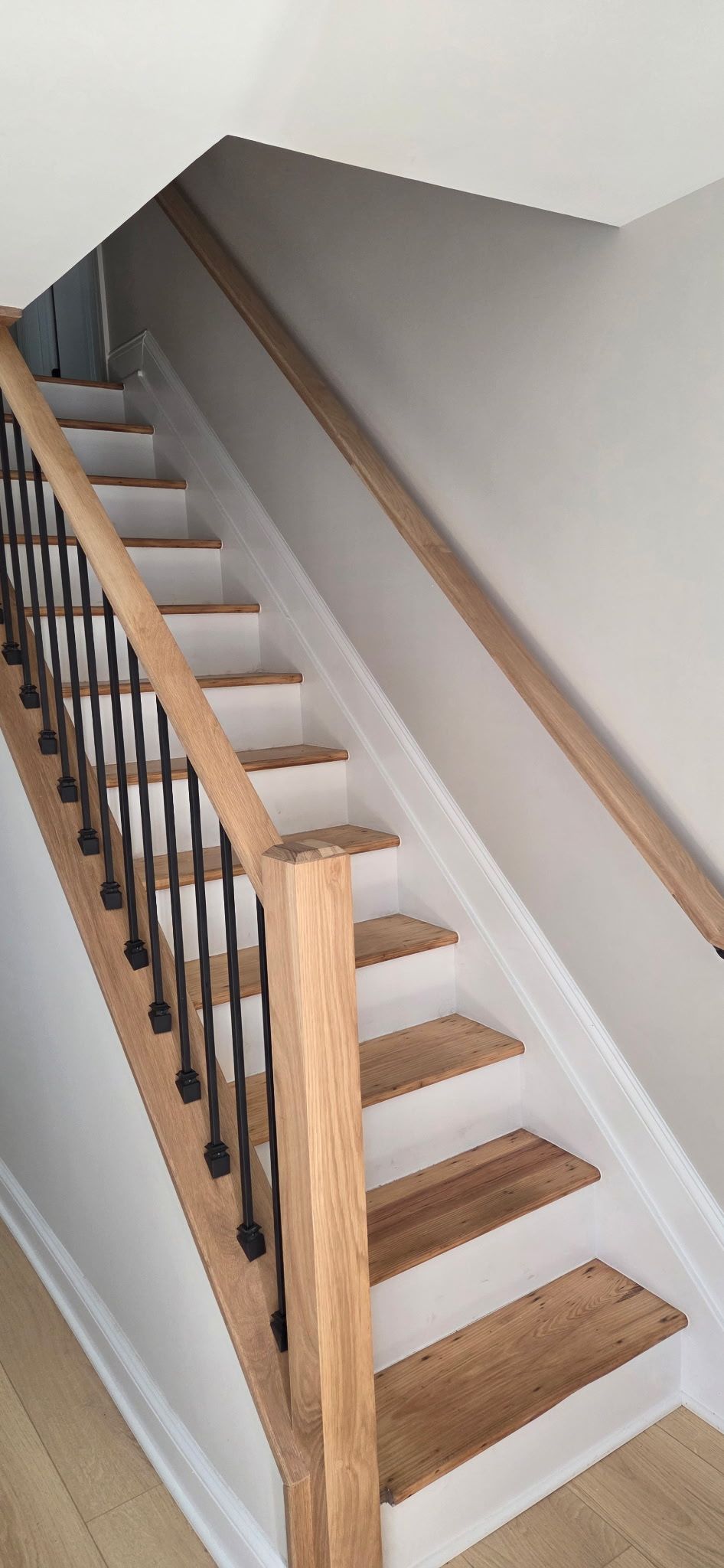 Wooden staircase with white risers, wooden treads, black spindles, and wooden handrails.
