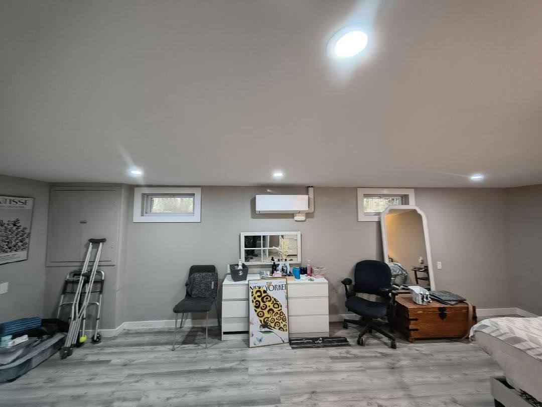 Room with gray walls, white dresser, chair, mirror, and air conditioner. Gray wood-look floor.
