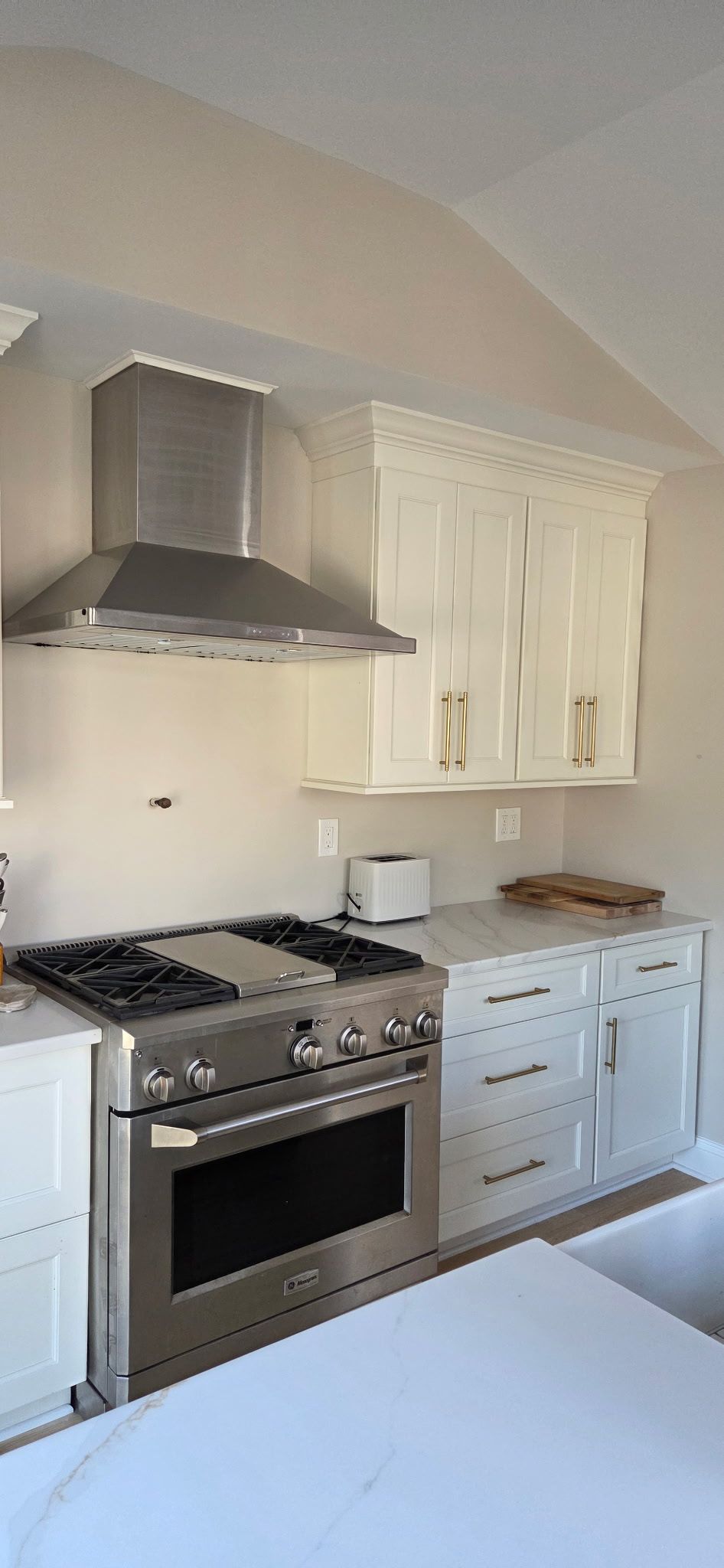 Kitchen with stainless steel range, hood, white cabinets, and countertops.