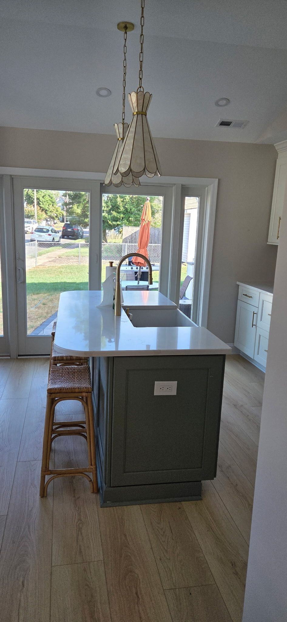 Kitchen island with white countertop, gray cabinets, sink, and pendant light fixture.