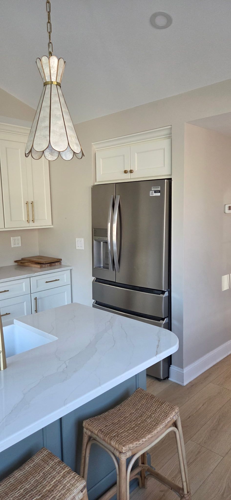 Kitchen with white countertops, stainless steel refrigerator, pendant light, and wicker stools.