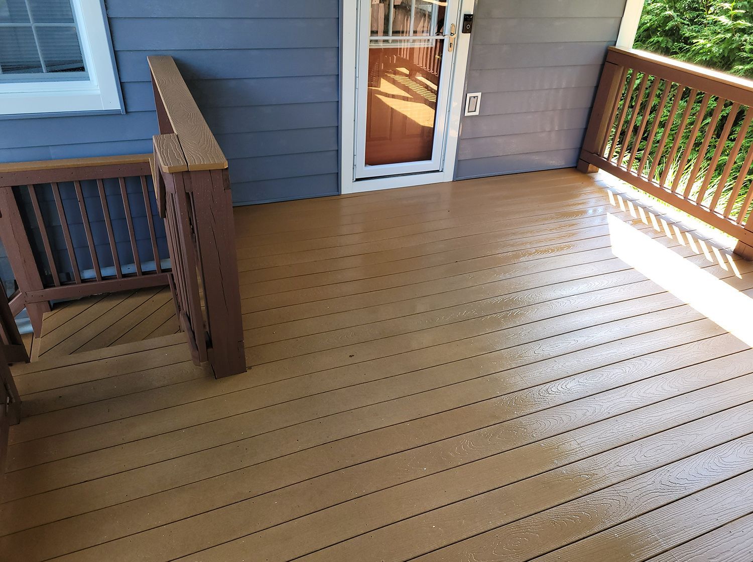 A wooden deck with a railing and stairs on the side of a house.